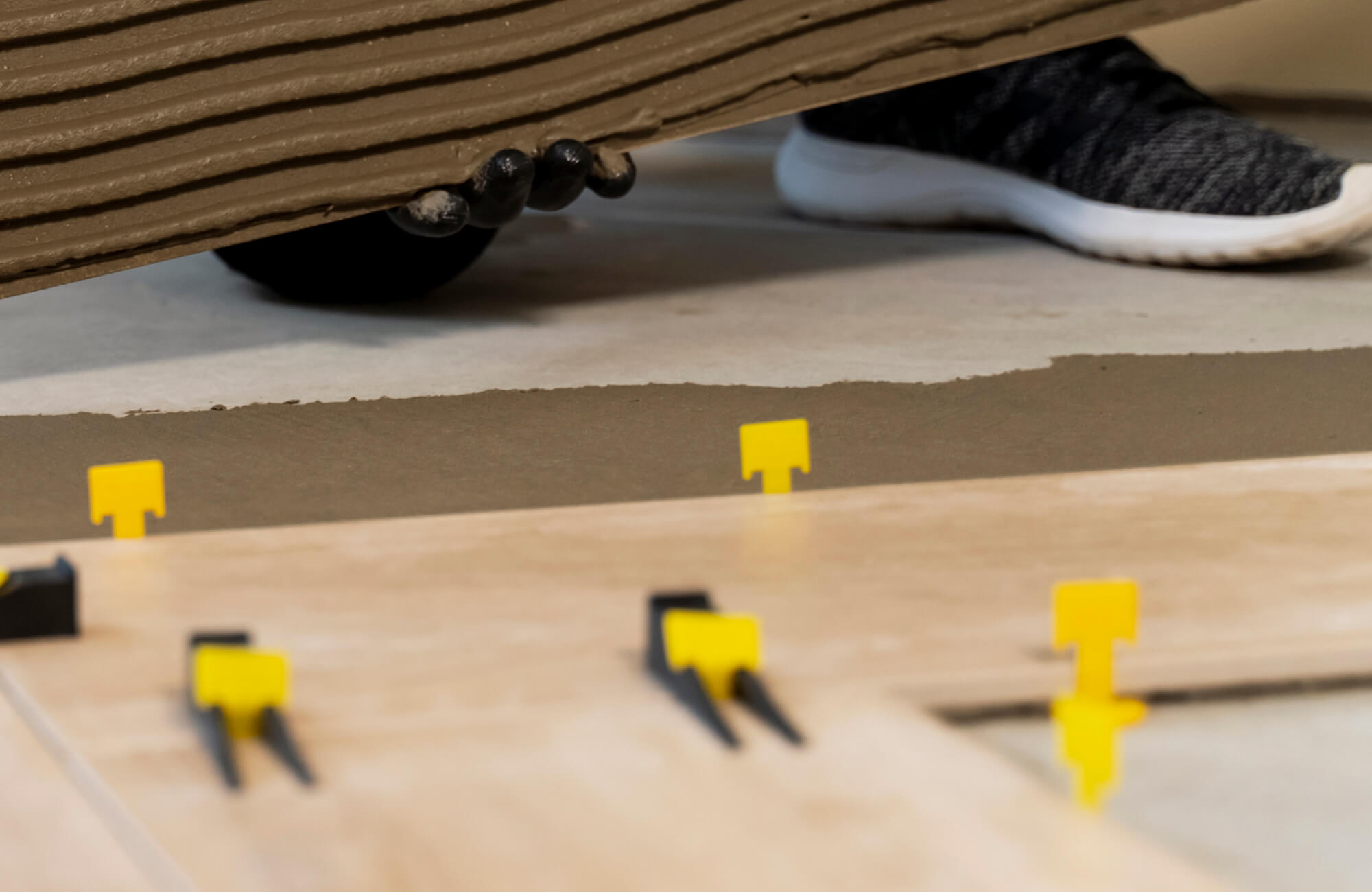 Worker positioning a tile over fresh mortar with leveling spacers during subway tile installation on a floor surface.