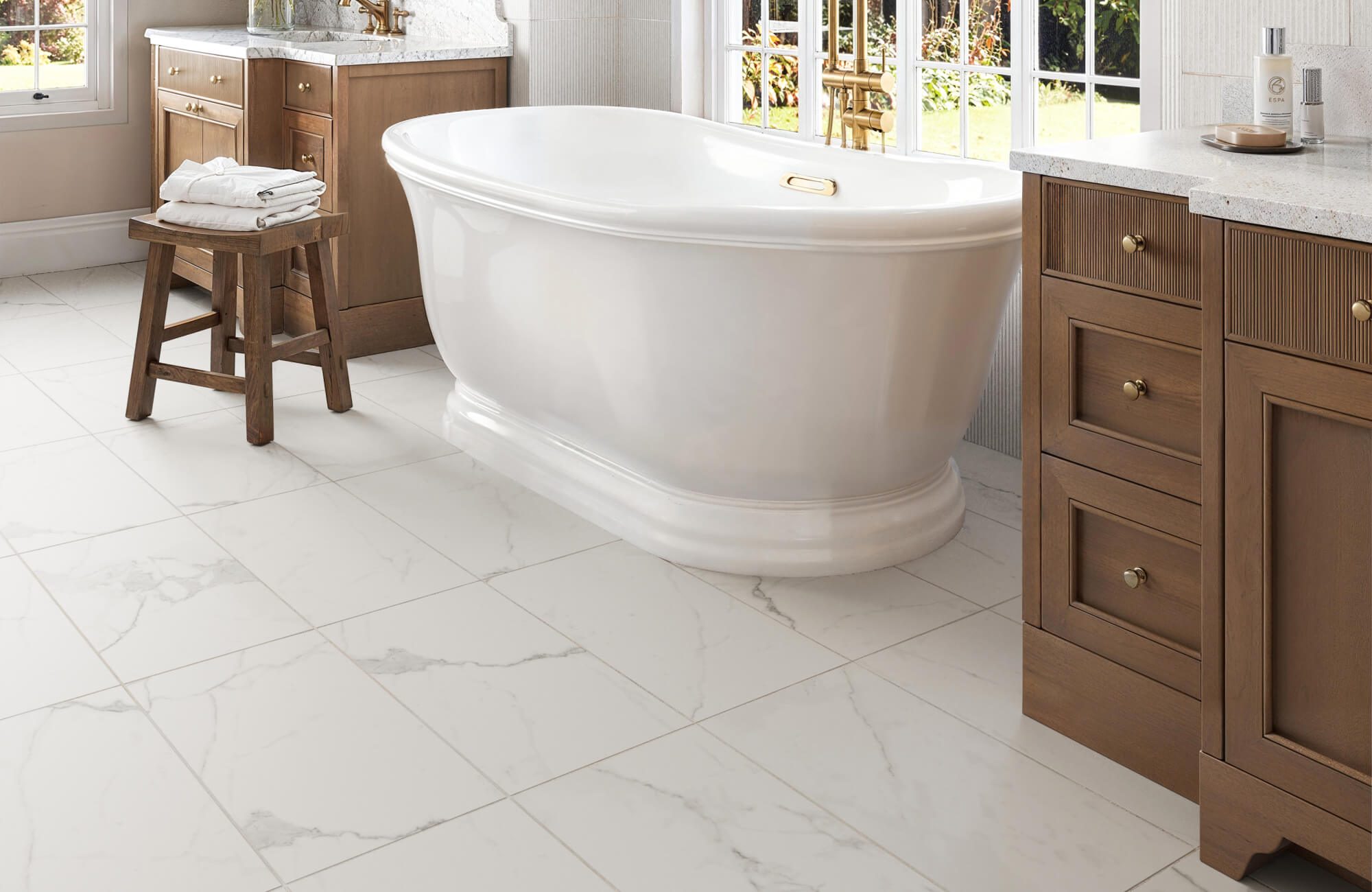 null A serene bathroom featuring a white freestanding tub, wooden cabinets, and elegant white marble look flooring with light veining, creating a luxurious spa-like atmosphere.