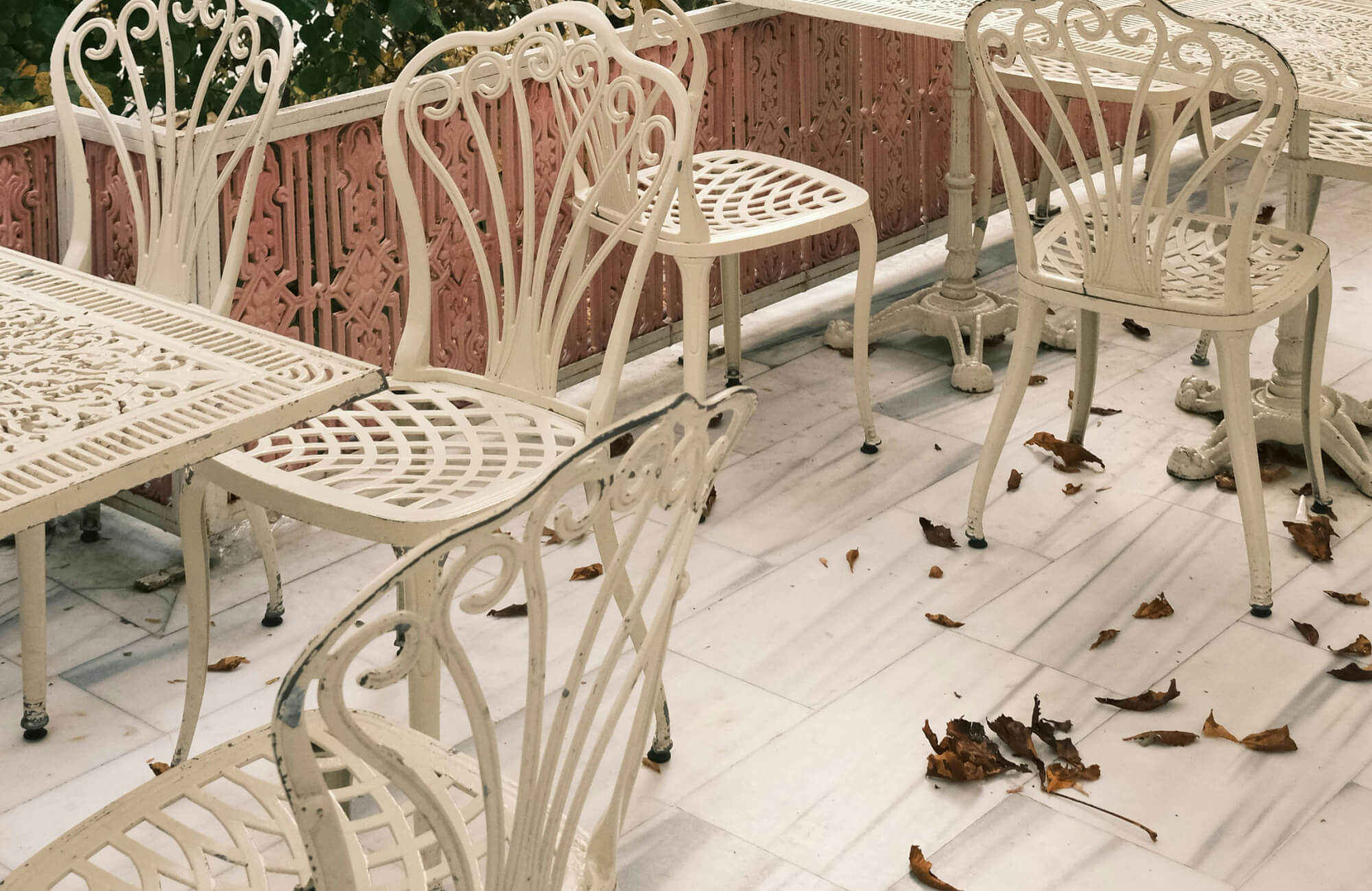 null Outdoor dining terrace with white metal tables and chairs on light marble flooring scattered with fallen leaves.