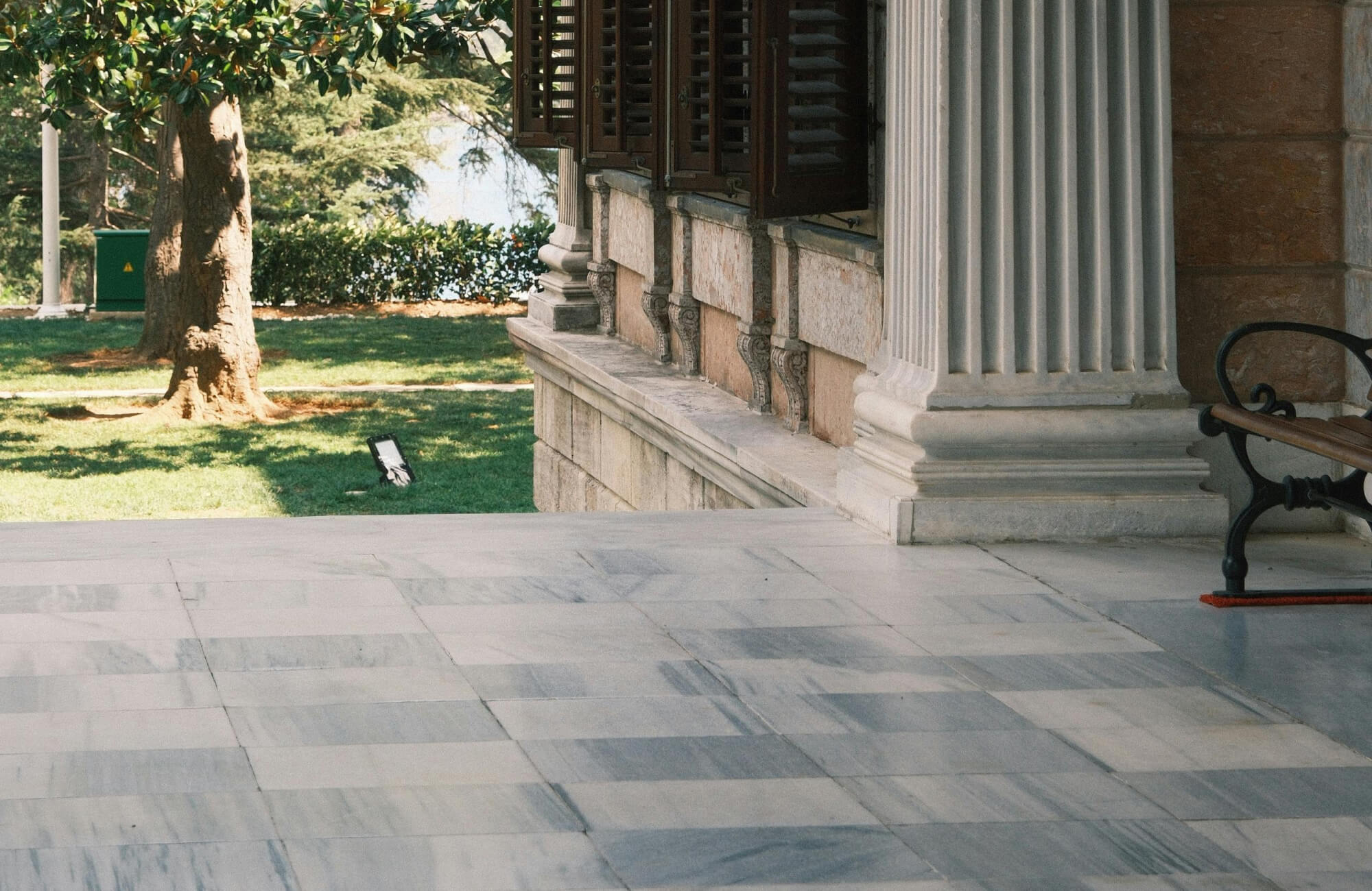 null Covered exterior walkway with marble tile flooring, stone columns, wooden shutters, and garden views.