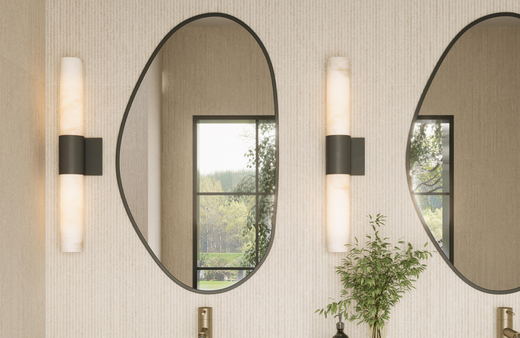 Modern bathroom with vertically mounted oval mirrors, wall sconces, brass fixtures, and a window view framed by light textured walls.