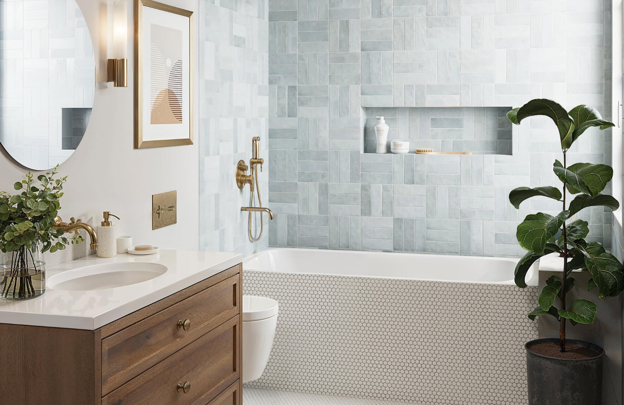 Contemporary bathroom with light blue herringbone wall tiles, white hexagon mosaic tub surround, brass fixtures, and a wood vanity.