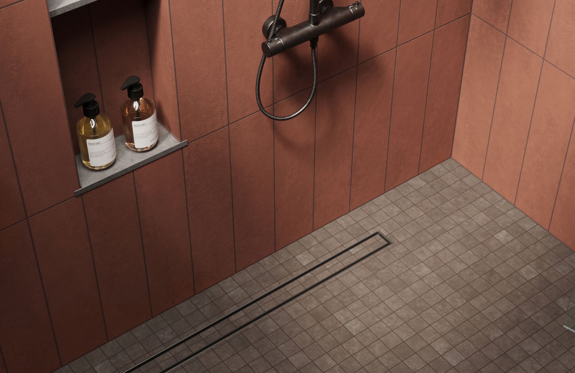 Modern shower with textured terracotta wall tiles, matte brown mosaic floor tiles, a linear drain, and a recessed shelf holding soap bottles.