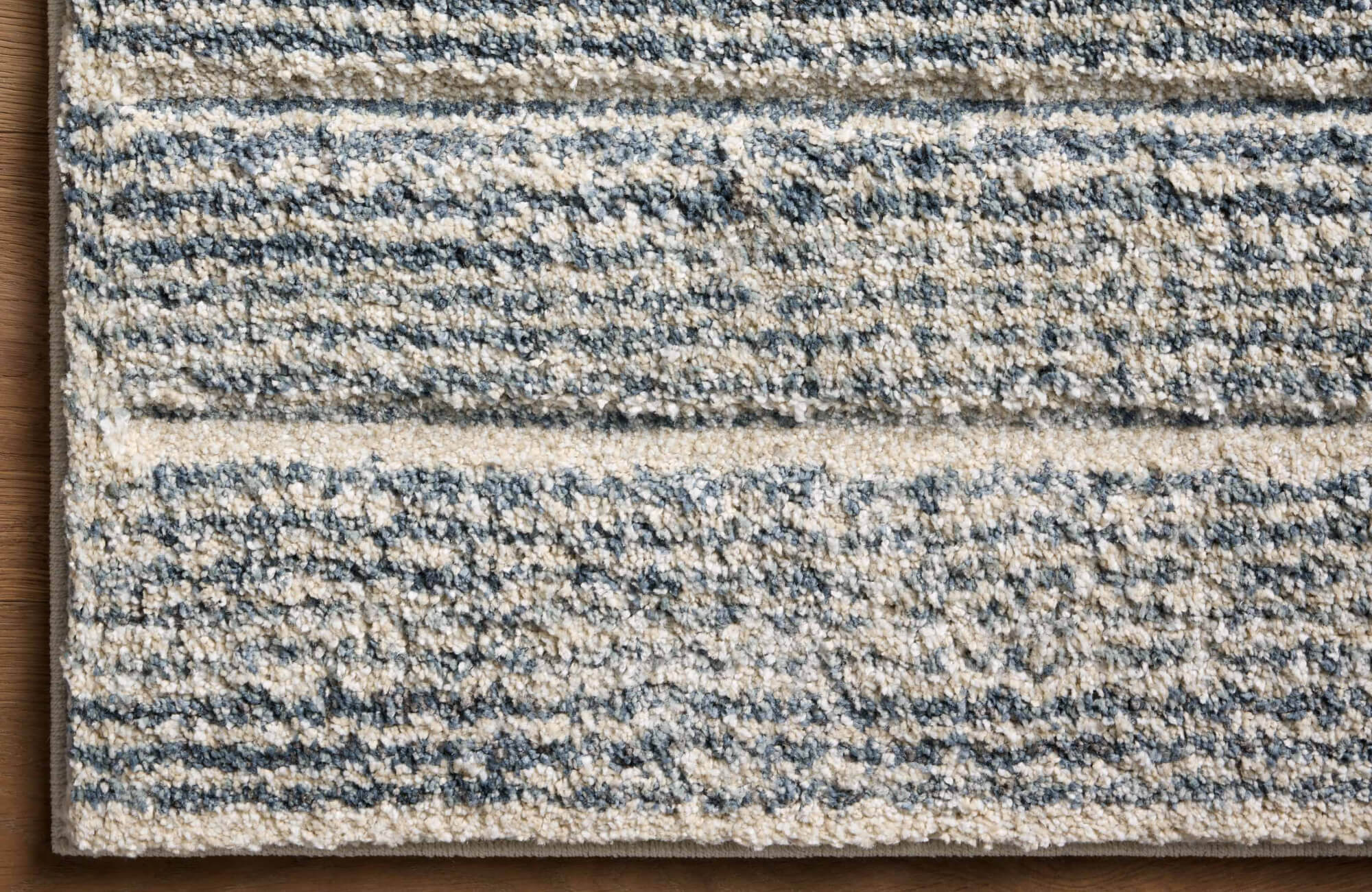 Close-up of a textured polypropylene area rug with a looped pile, featuring a soft blend of cream and blue-gray horizontal striations.