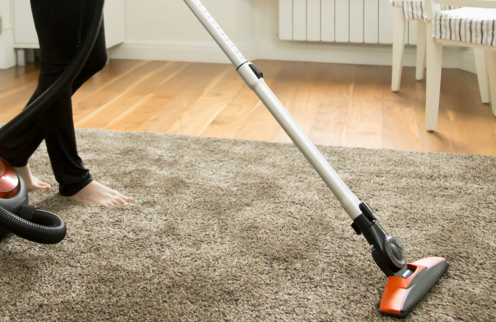 Person vacuuming a soft taupe polypropylene rug in a cozy home setting with wood floors and minimal furniture.