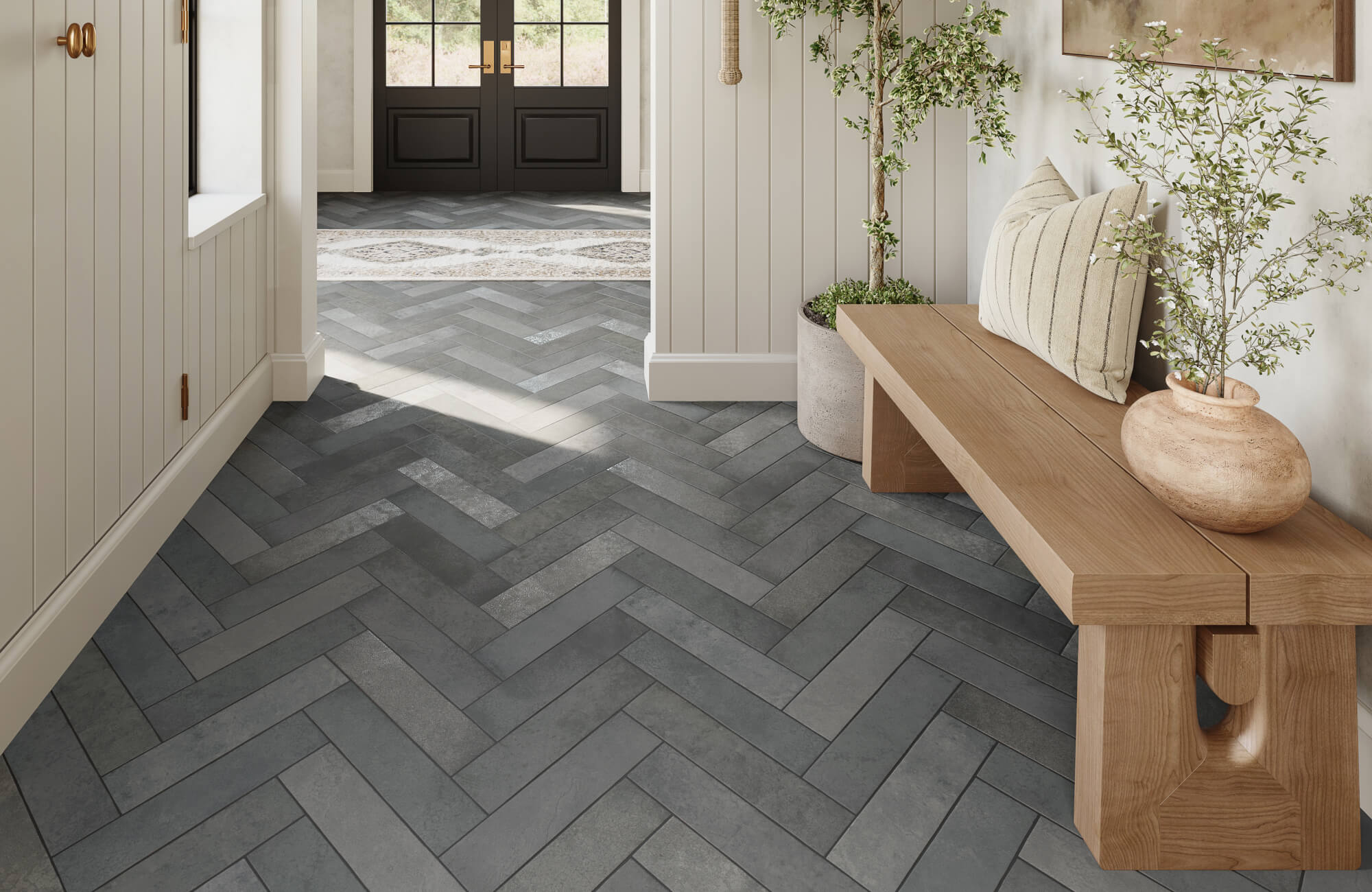 Herringbone-patterned tile flooring in deep gray tones, creating visual movement beneath a minimalist bench and indoor plants.