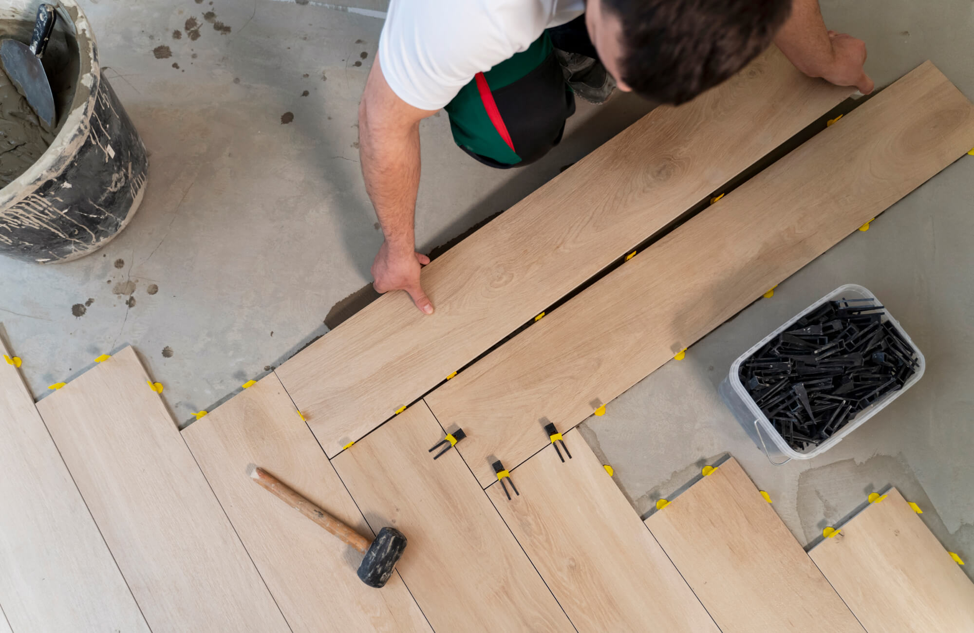 Overhead view of herringbone tile installation in progress, showing precise plank placement, leveling clips, and tools.