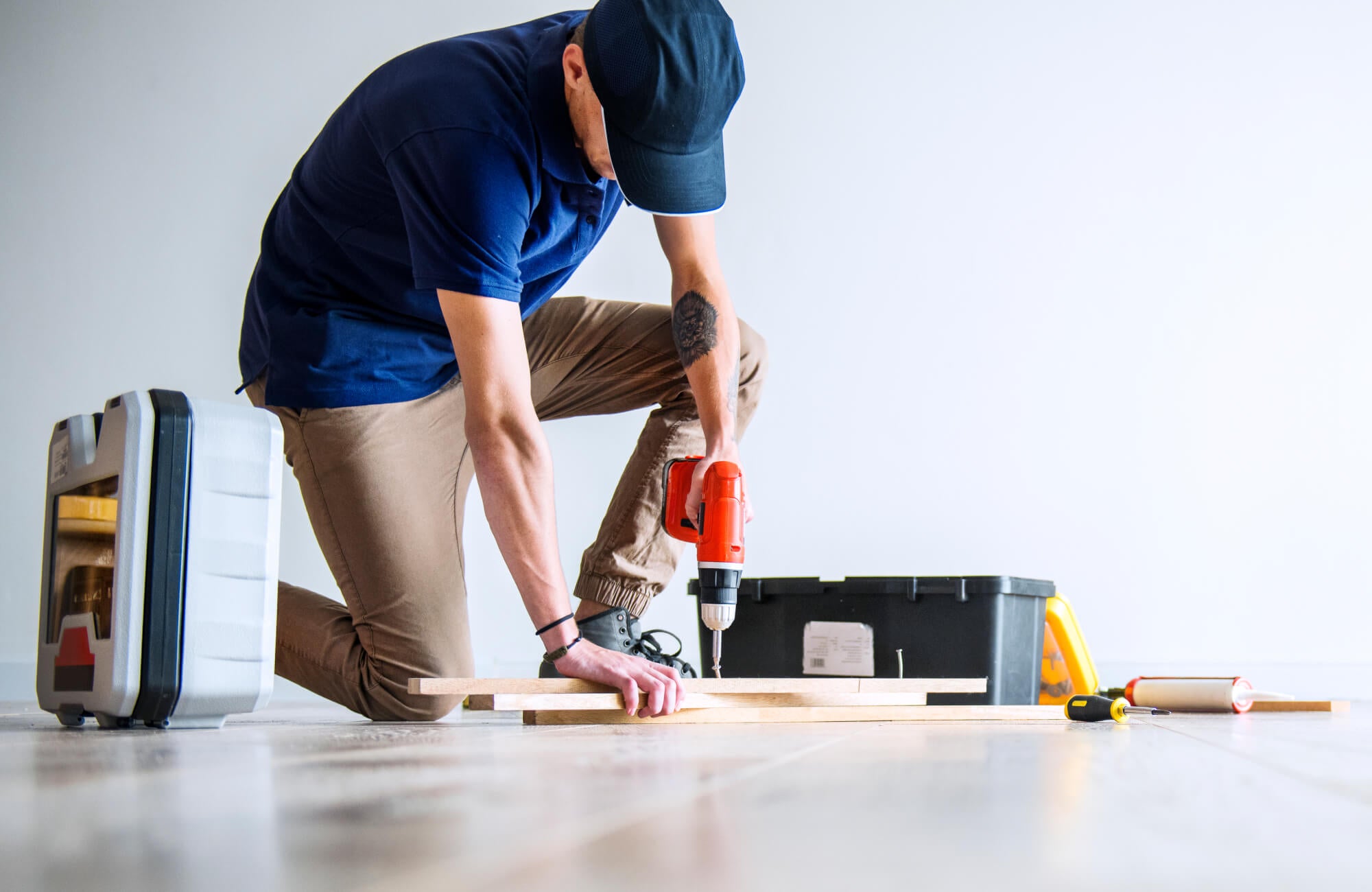 DIY flooring work in progress, showing plank alignment and tools laid out on a bare floor.