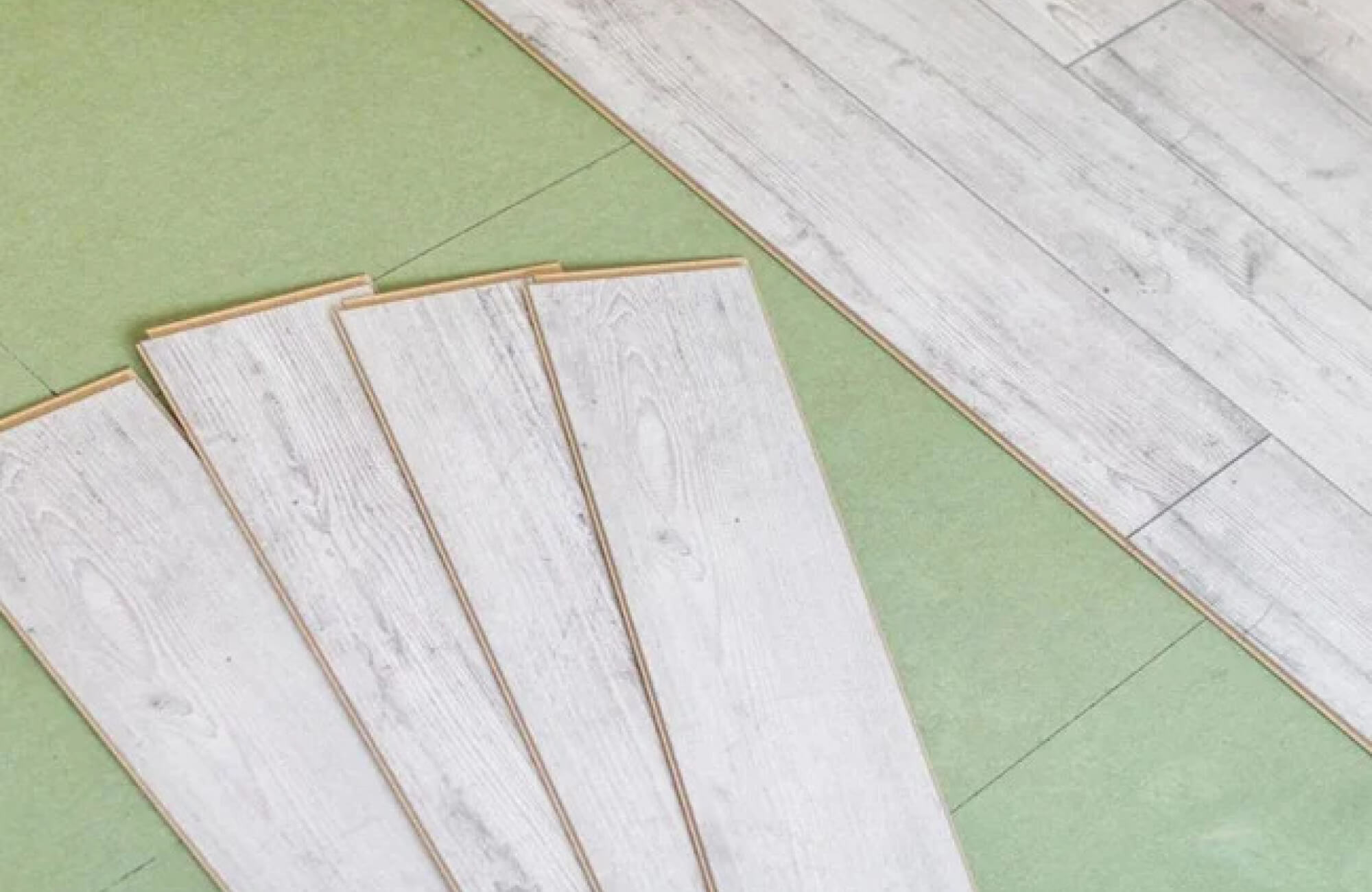 null Light gray wood look laminate planks being installed over a green underlayment, ensuring a smooth and cushioned flooring finish.