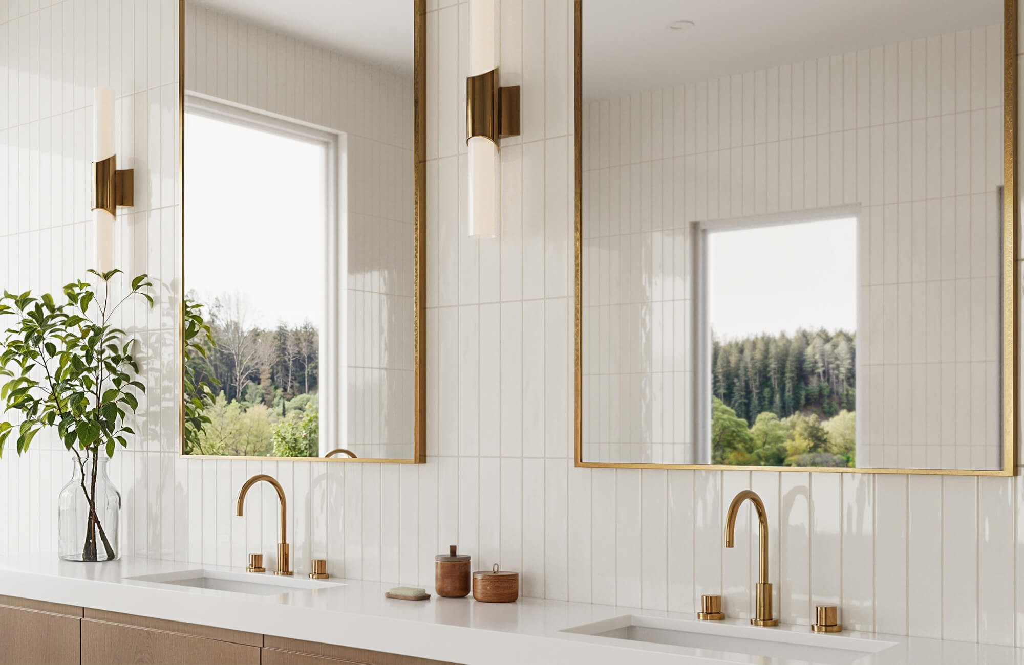 null Bright double vanity bathroom with glossy vertical white rectangular wall tiles, brass-framed mirrors, gold faucets, white countertops, light wood cabinetry, and large windows facing a wooded view.