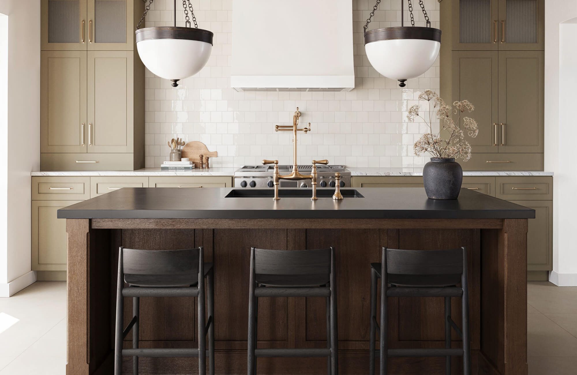 null Traditional kitchen with glossy square white backsplash tiles, olive-taupe cabinetry, brass hardware, black island countertop, dark wood island, oversized pendant lights, and black counter stools.