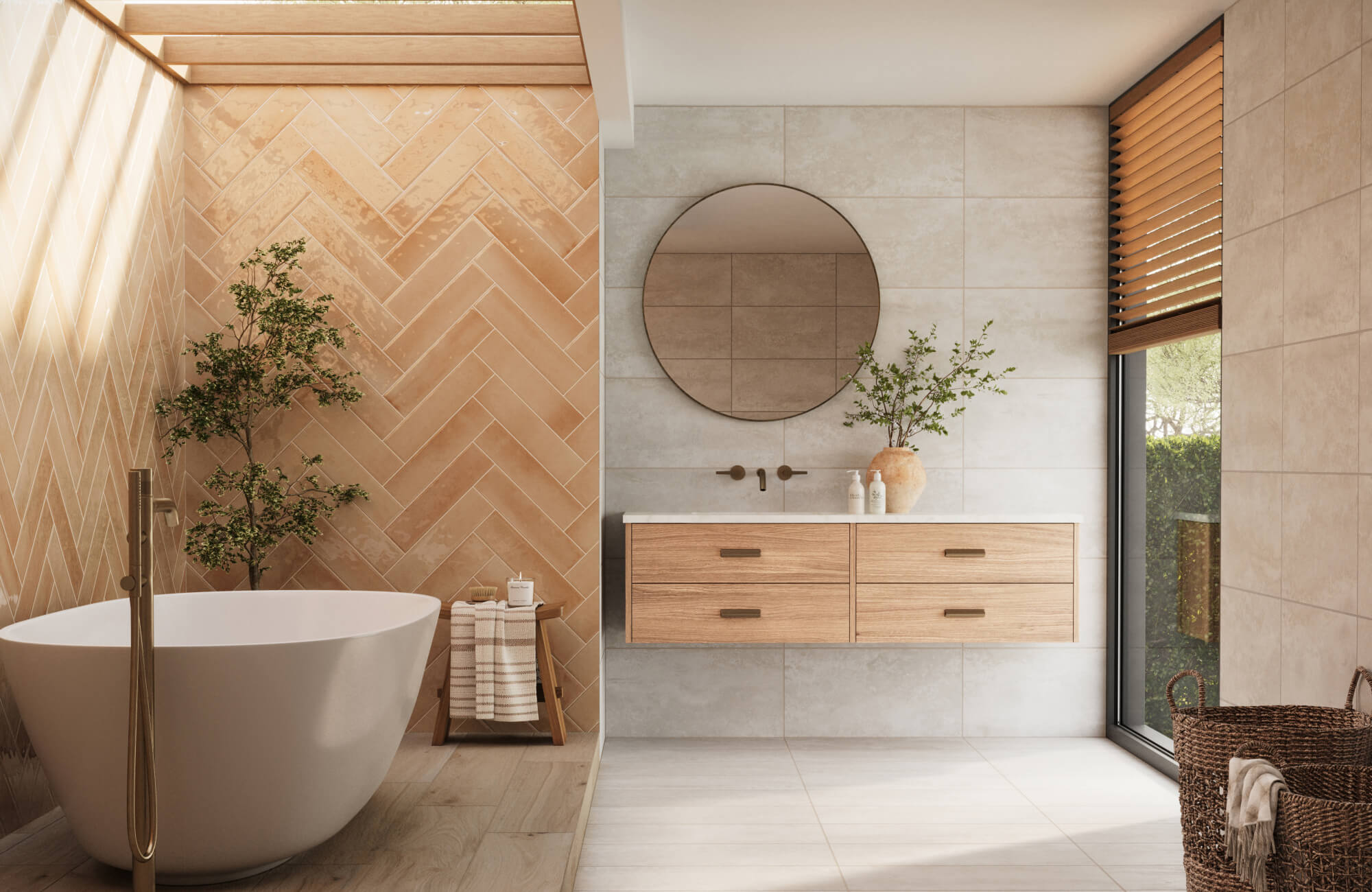 null Spa-like bathroom with glossy terracotta herringbone wall tiles, a white freestanding tub, brass floor-mounted faucet, pale stone-look walls, wood vanity, round mirror, woven basket, and filtered daylight.