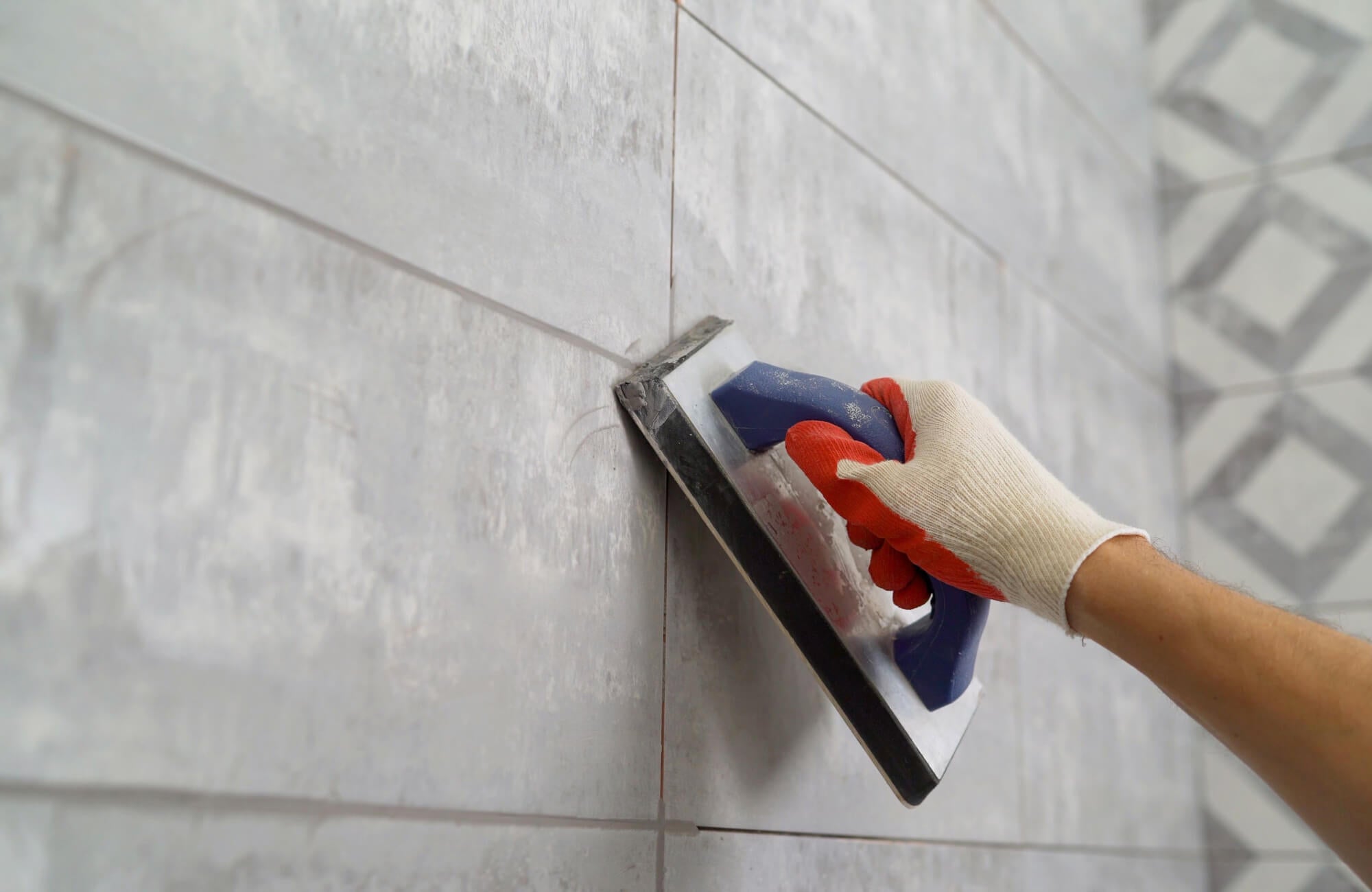 null Close-up of a worker applying grout to gray wall tiles using a grout float, wearing protective gloves during tile installation.