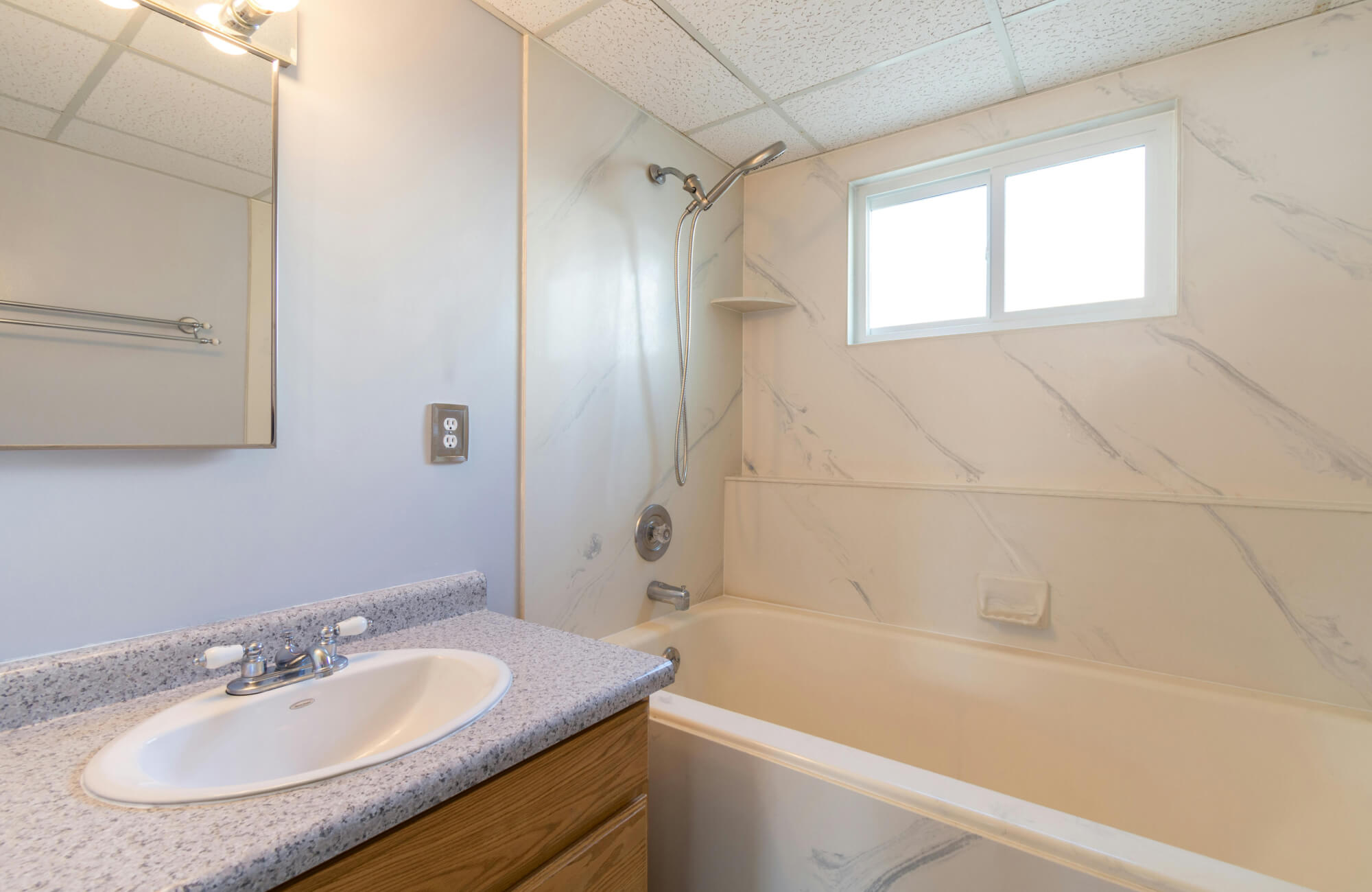 null Small bathroom with marble look shower wall panels, bathtub, window, and compact vanity demonstrating a practical marble style design.