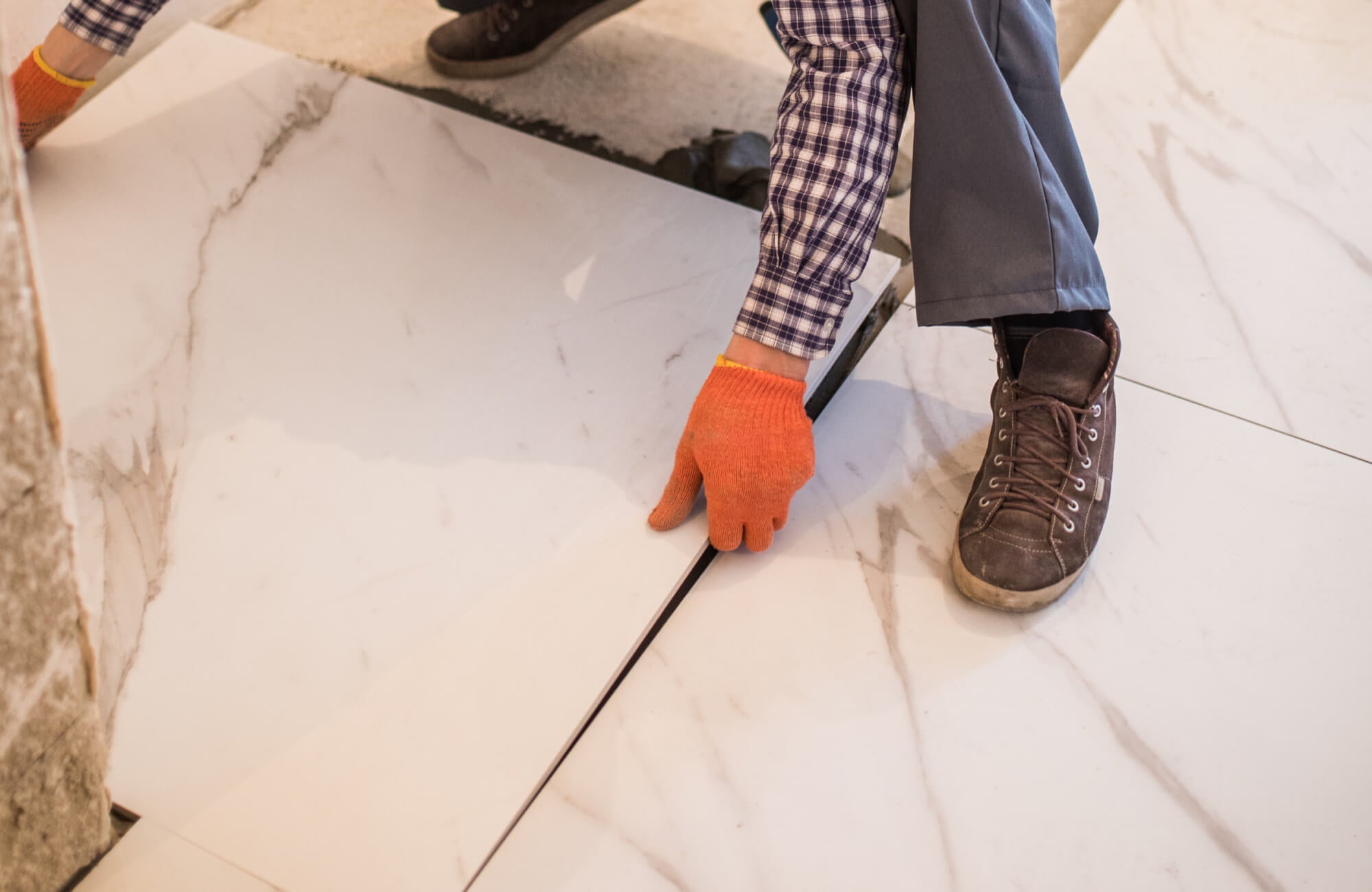null Installer positioning large marble look porcelain tiles on the floor during bathroom renovation, showing realistic Carrara marble veining.