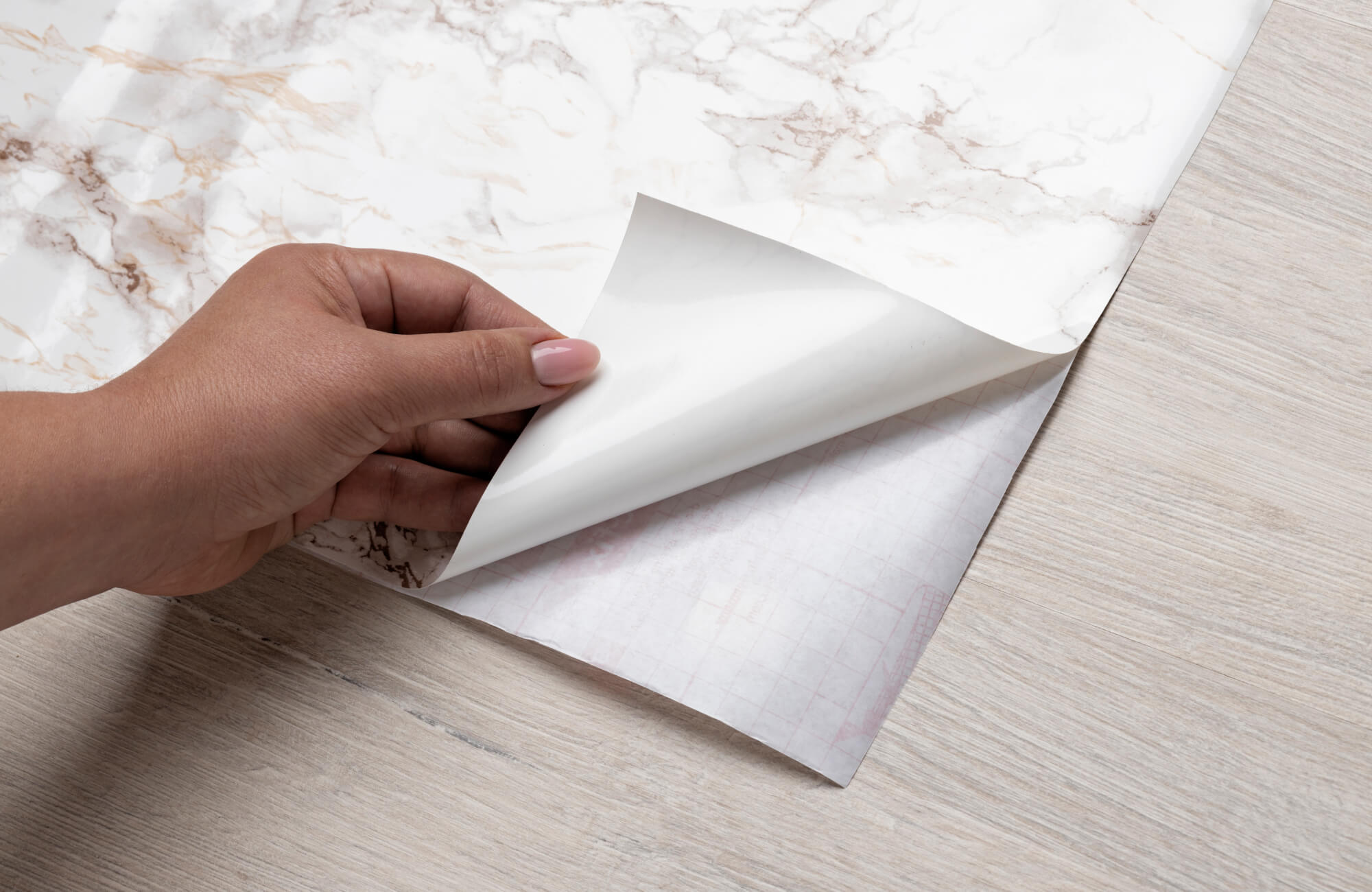 A close-up of a hand peeling adhesive tile backing, illustrating the simplicity of peel-and-stick tile installation.