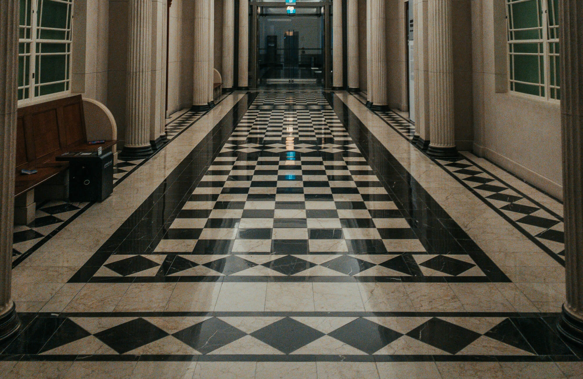 Grand hallway featuring an intricate black and light brown checkered tile pattern, flanked by classic columns and accentuated with luxurious marble details