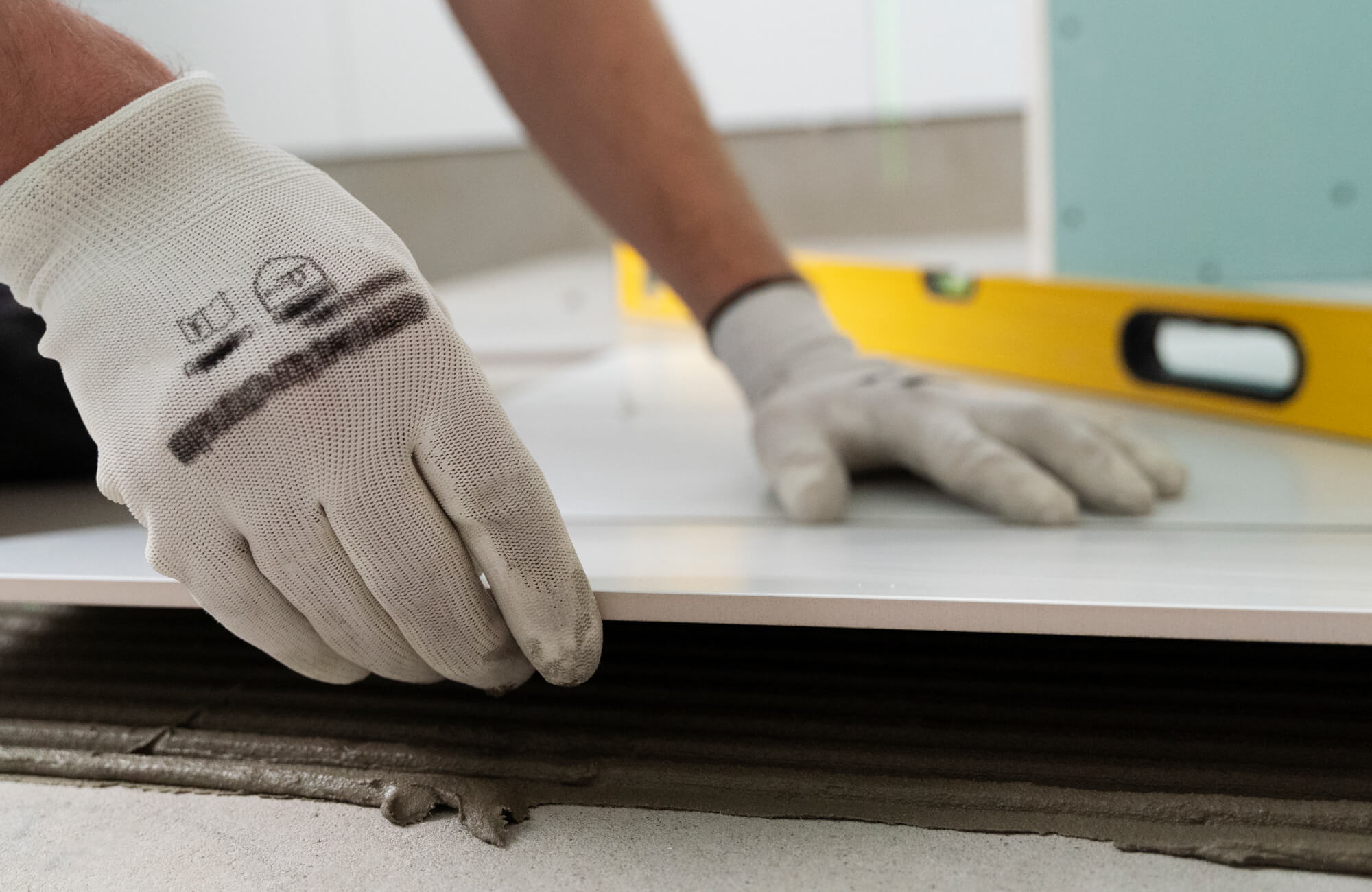Close-up of a worker's gloved hands carefully placing a large tile into adhesive mortar, highlighting the precision and craftsmanship in checkered tile installation