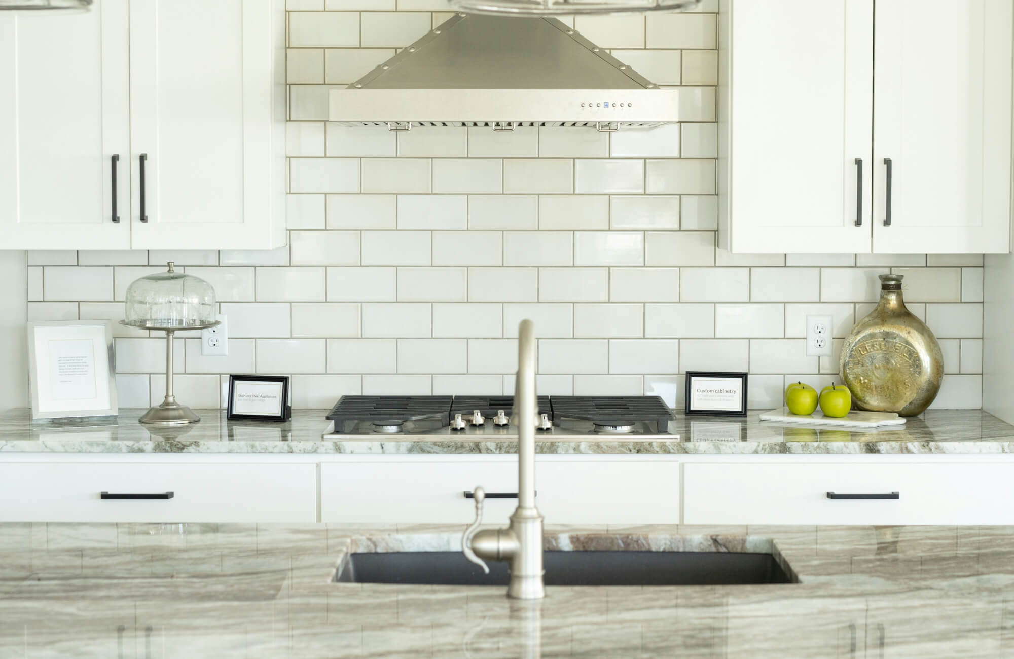 Modern kitchen with white glossy 3x6 subway tile backsplash in a classic brick pattern, paired with white cabinets, marble countertops, and stainless steel range hood.