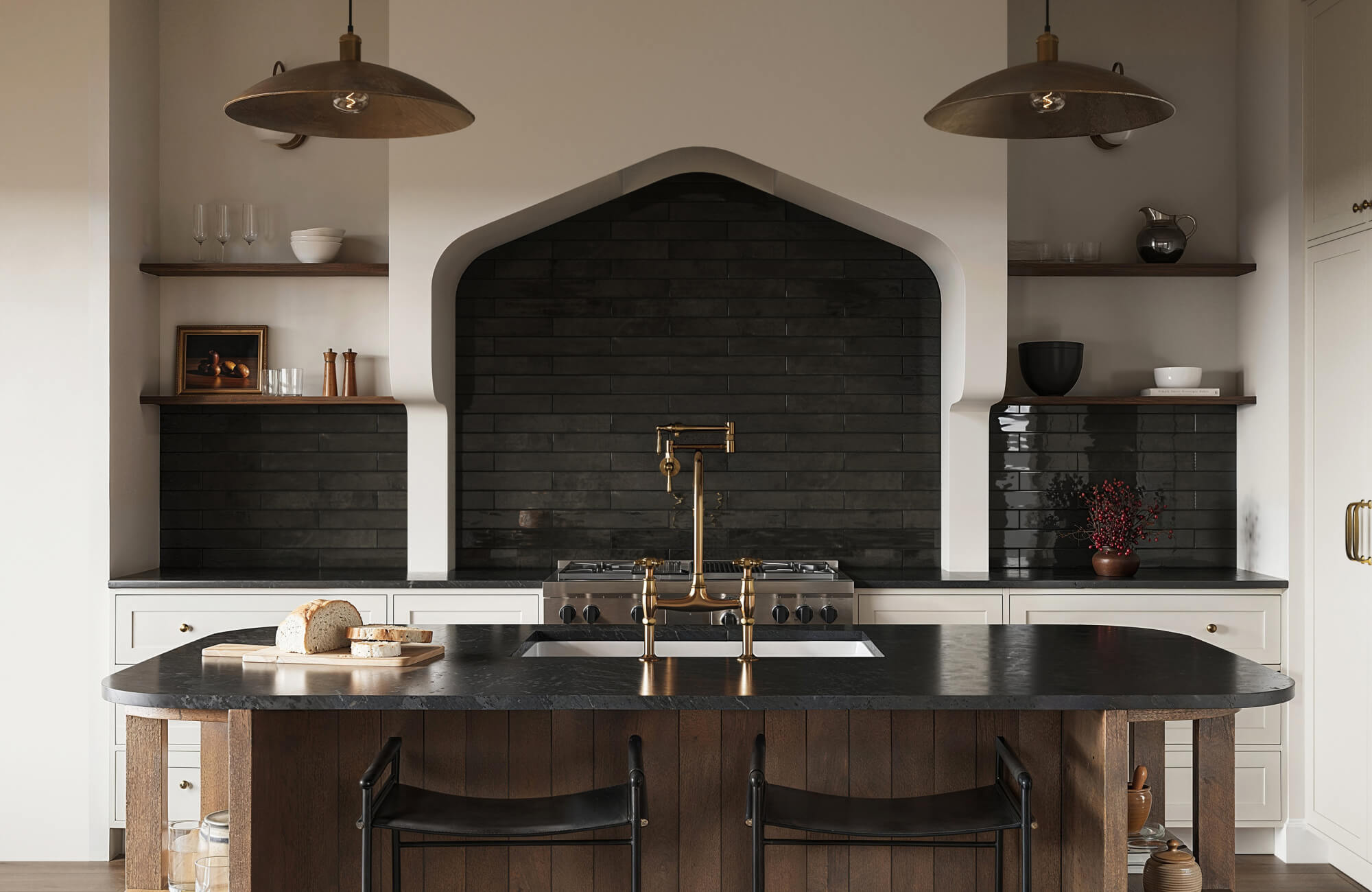 Luxury kitchen with long glossy black subway tile backsplash in a horizontal layout, paired with white cabinetry, brass fixtures, arched range hood niche, and dark wood island.
