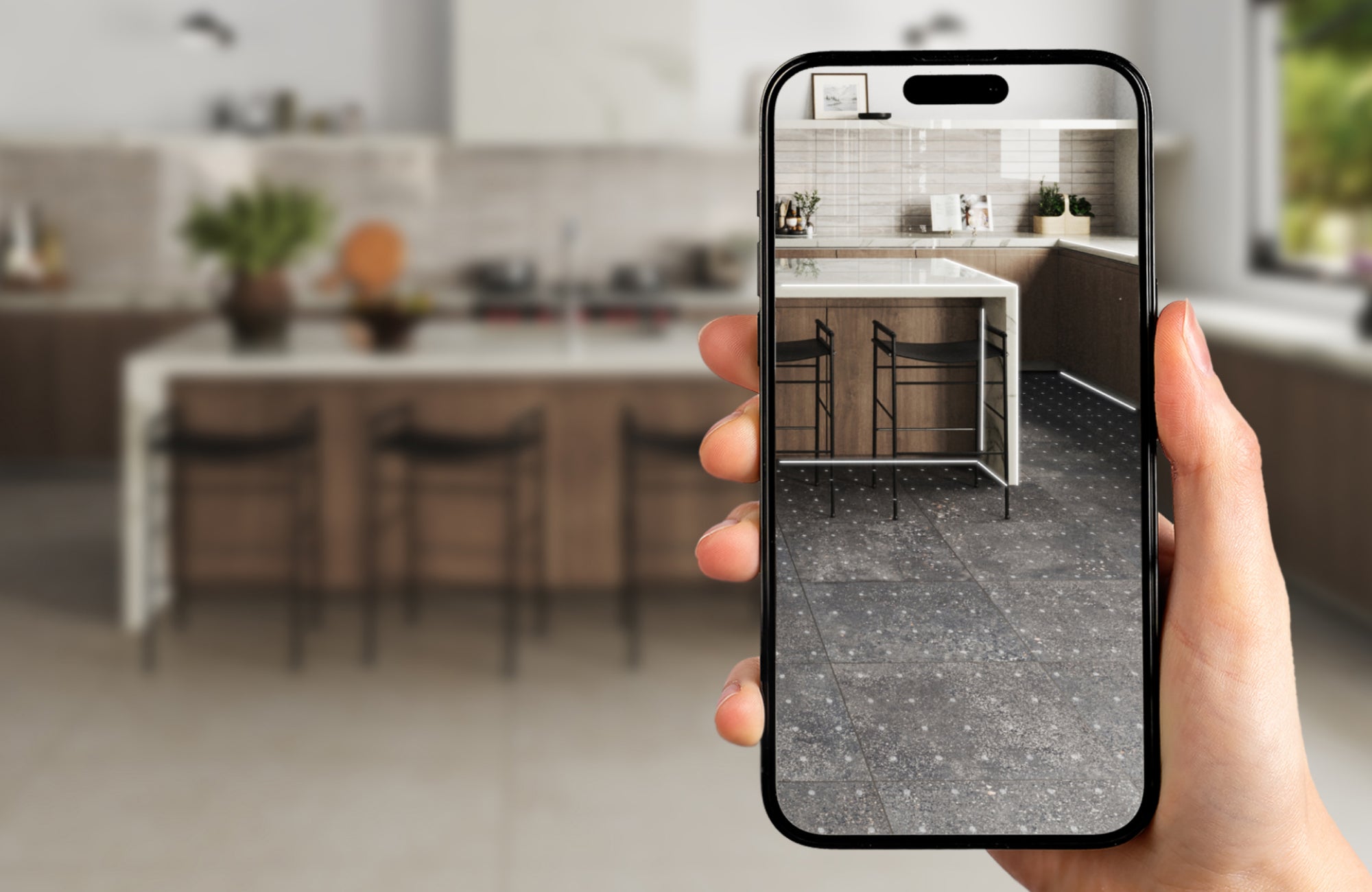 Hand holding phone with AR tile visualizer showing dark speckled tiles in a modern kitchen for layout previewing.