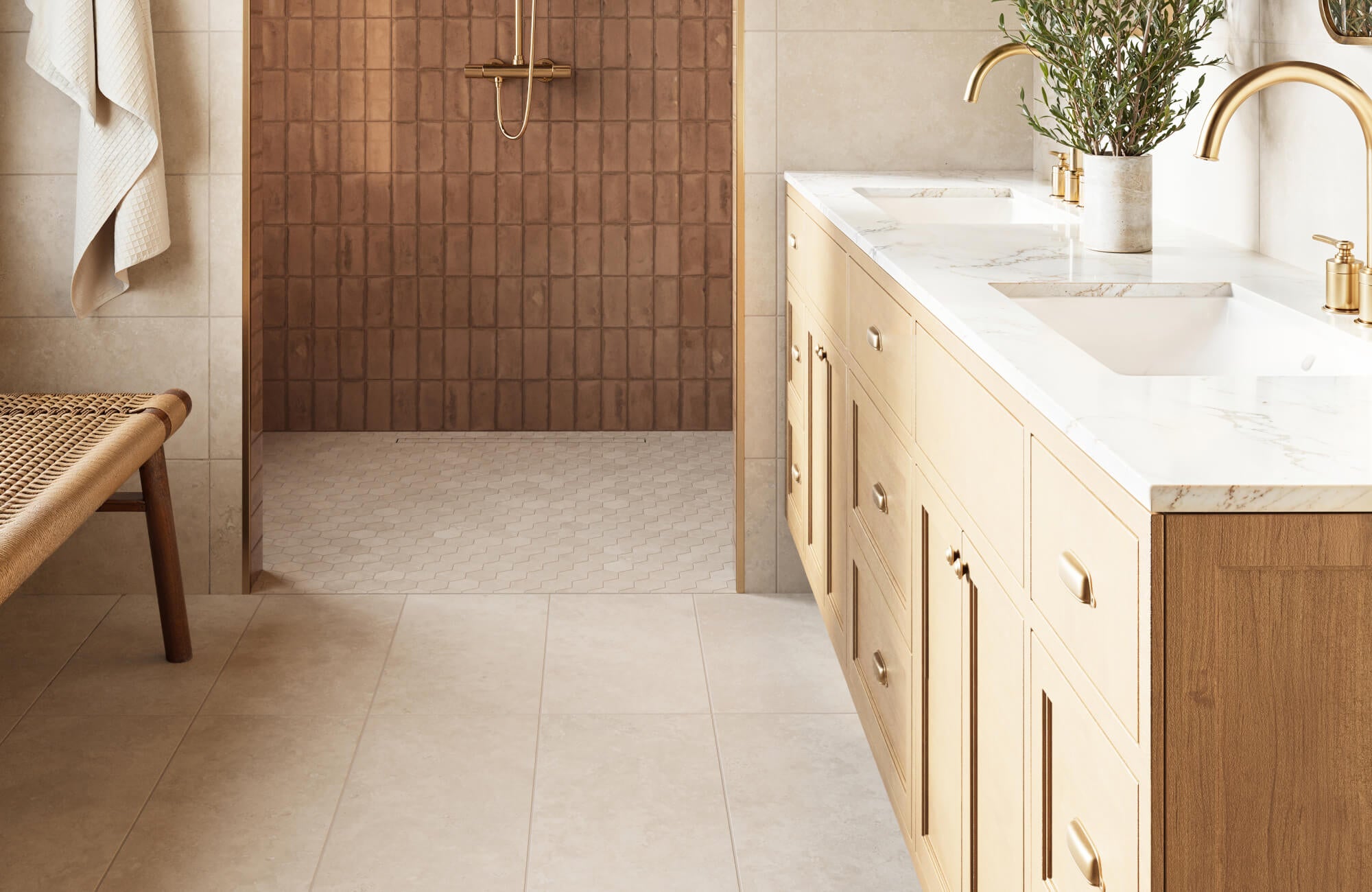 Warm neutral bathroom tile design featuring textured brown bathroom wall tiles in the shower, hexagon bathroom floor tiles, and large format beige floor tiles paired with a wood vanity and brushed gold fixtures.