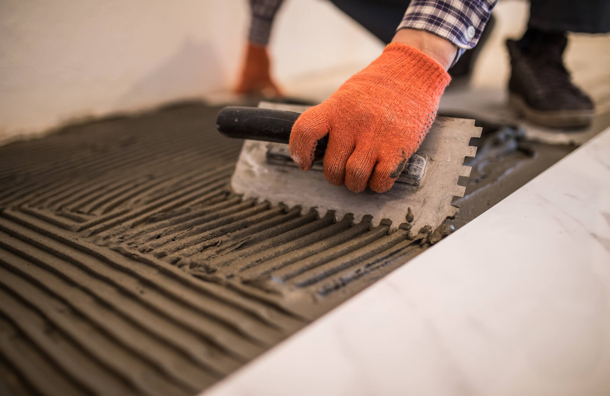 Bathroom tile installation process showing adhesive being applied with a notched trowel for bathroom floor tiles, highlighting proper tile installation techniques and surface preparation.