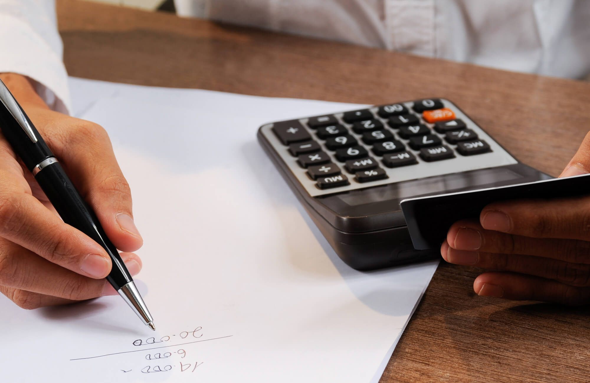 null A person calculates expenses with a calculator and notes on paper while holding a credit card, illustrating budgeting and cost planning as a key step in any bathroom renovation.