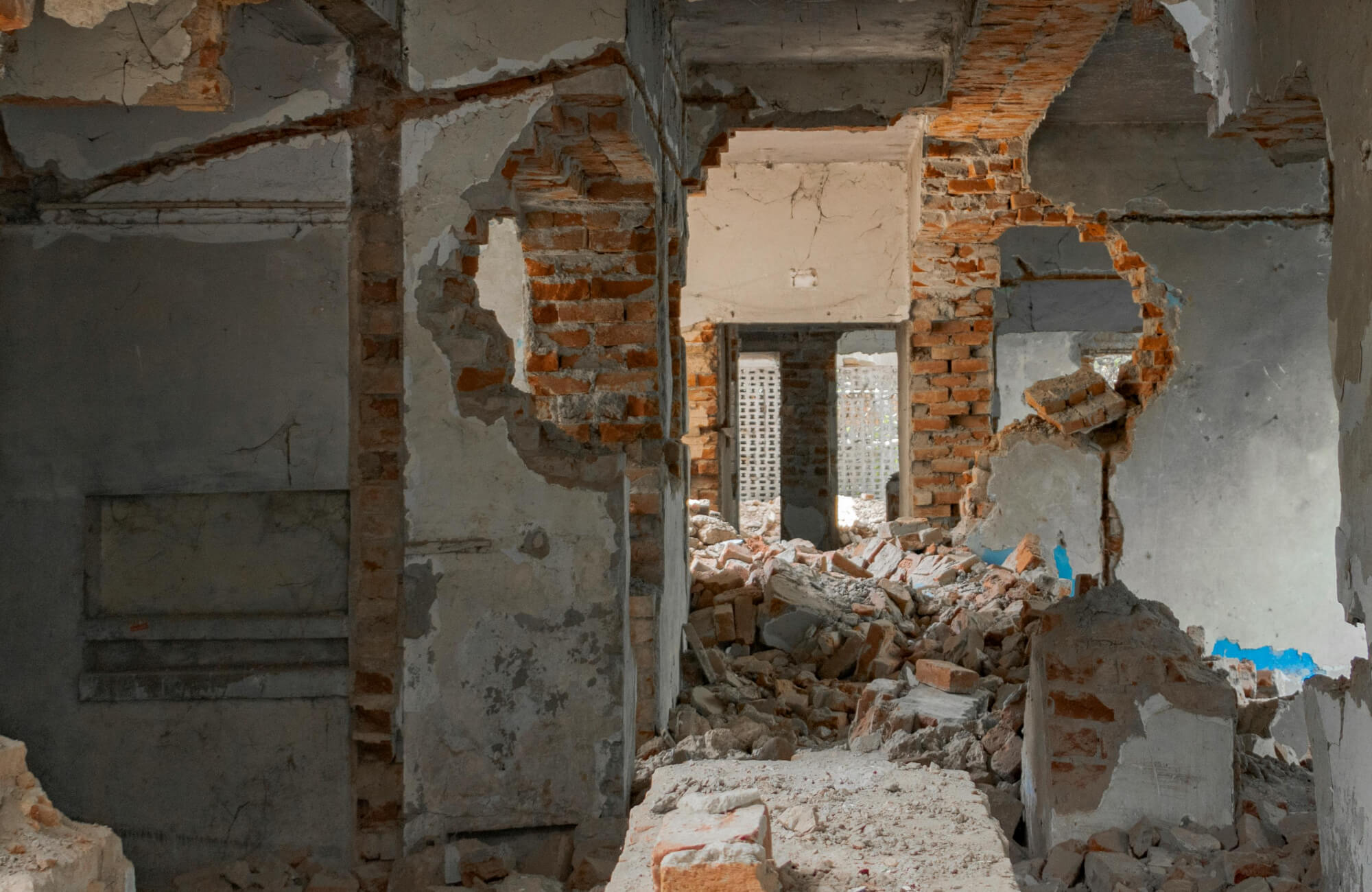 null An interior space mid-demolition with exposed brick walls, broken plaster, and scattered rubble captures the early teardown phase of a major bathroom renovation.