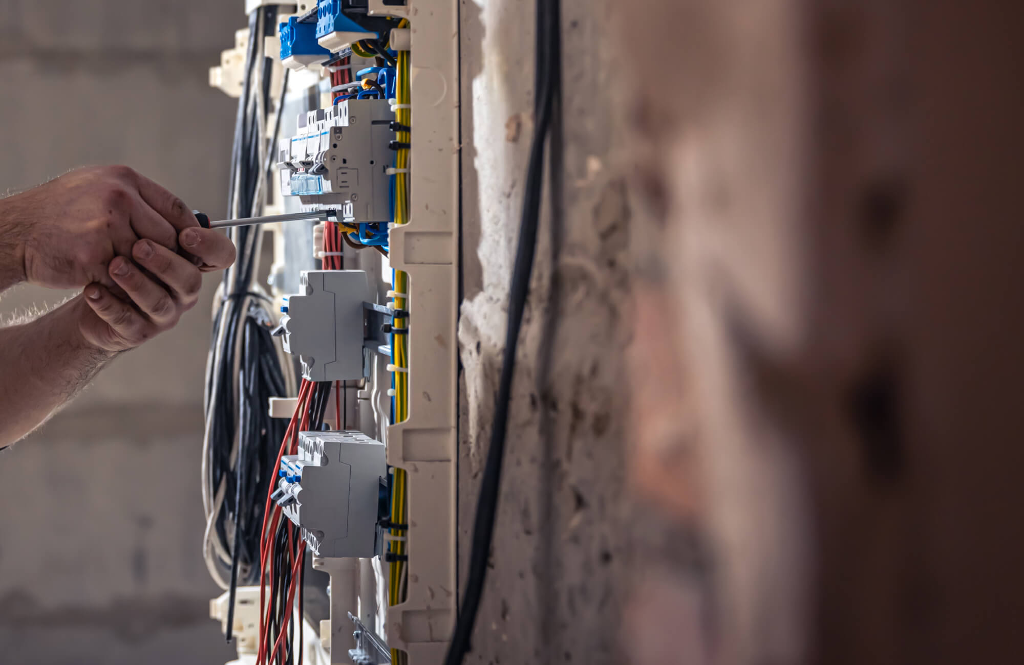 null Electrician tightening wiring inside an electrical panel during a bathroom renovation, showing circuit breakers, organized cables, and in-wall electrical work.
