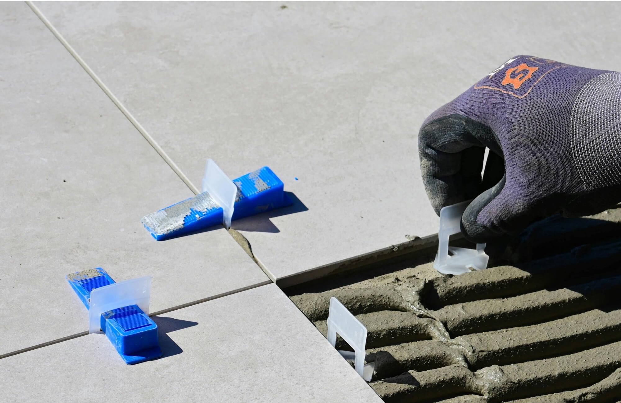 null A worker carefully places leveling clips and spacers between large-format tiles set in fresh mortar, demonstrating the precision workmanship essential to a professional bathroom renovation.
