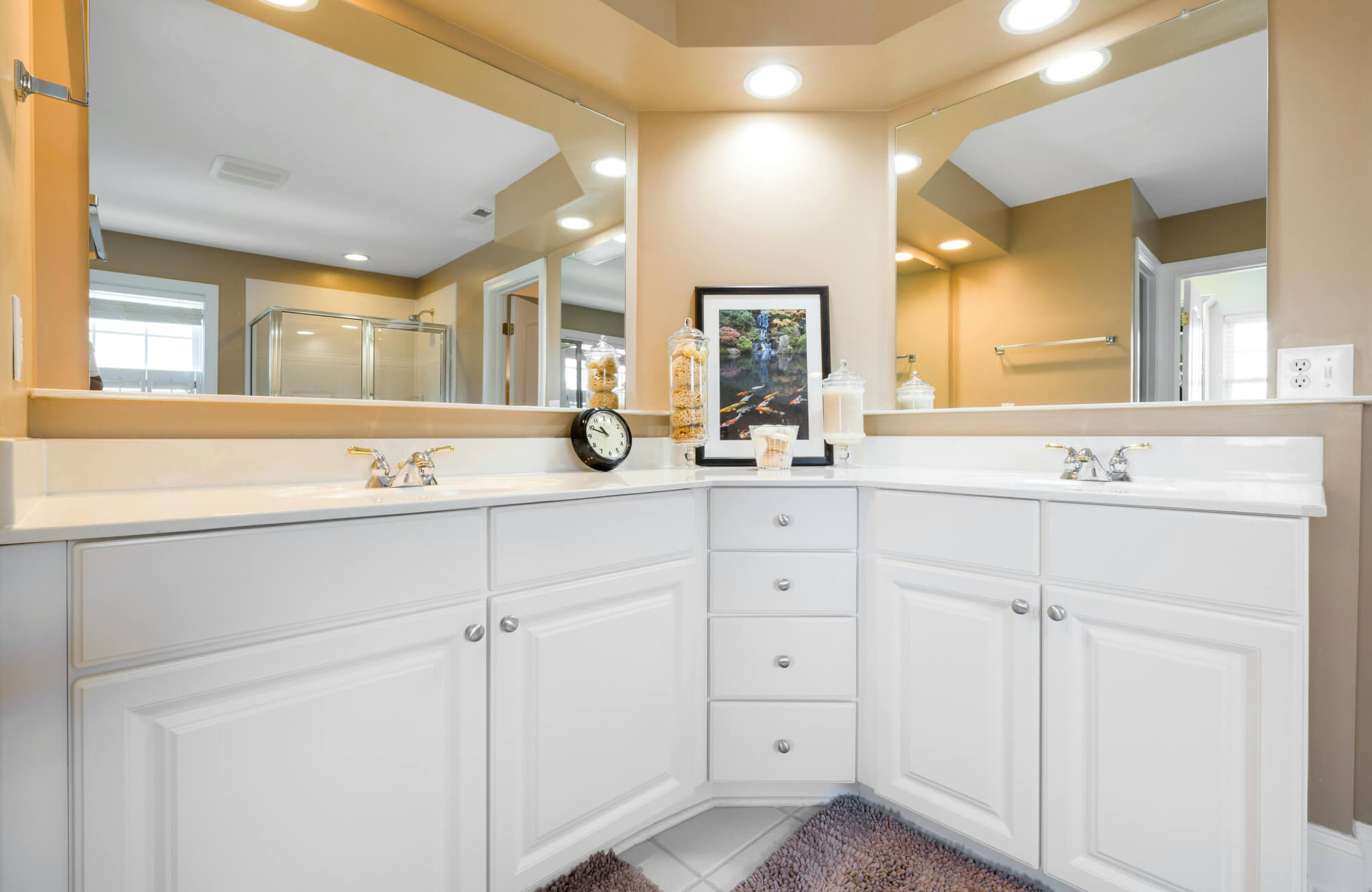 null White double corner vanity with two sinks, wide mirrors, and ample cabinet storage in a spacious shared bathroom.