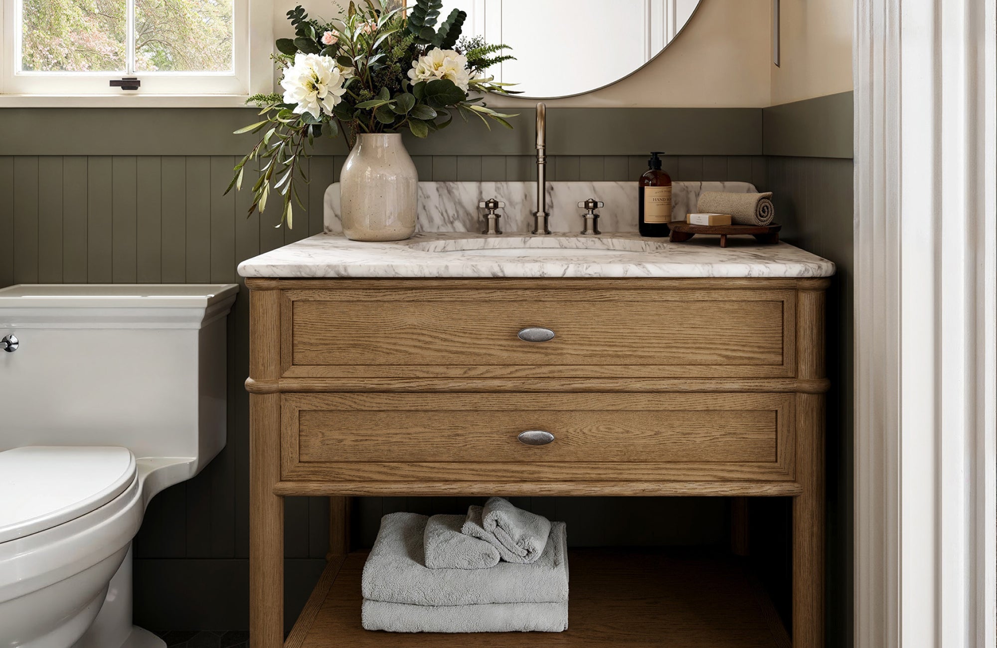 null Compact vanity with marble top, two drawers, and open shelf, styled with flowers in a cozy traditional bathroom.