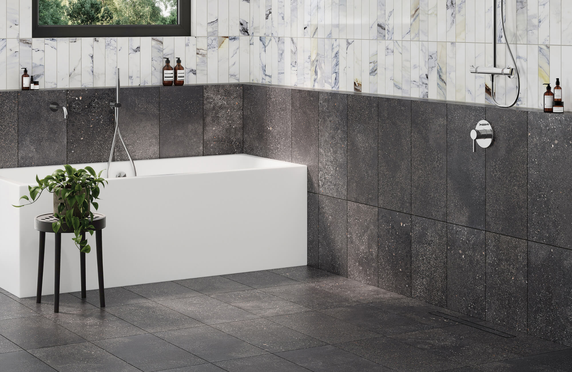 Contemporary bathroom with speckled black wall and floor tiles, a white soaking tub, marble accent wall, and a small black stool with greenery.