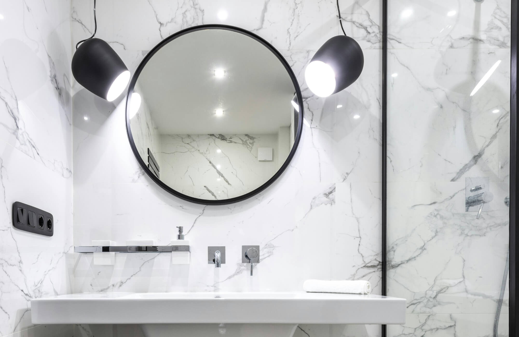 null Contemporary bathroom featuring a black-framed mirror, sleek wall-mounted faucet, and marble-style tiles with soft pendant lights.