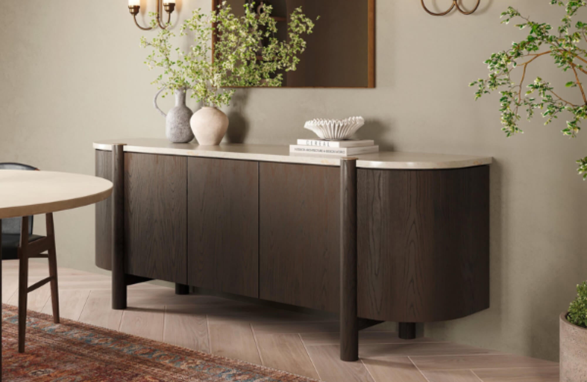 Dining area with soft wood herringbone flooring, curved dark wood sideboard, neutral walls, and organic decor for a calm, cohesive feel.