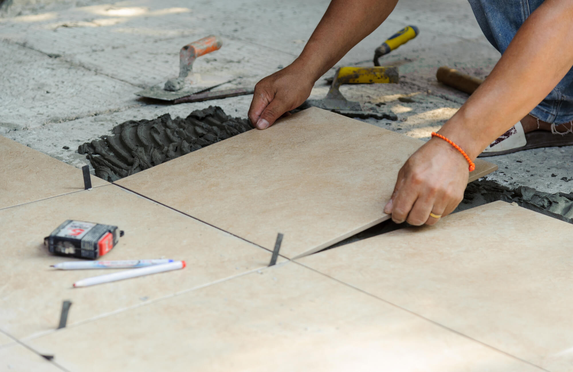Worker installing large beige floor tiles with spacers and mortar, using precise alignment tools for even spacing and level placement.
