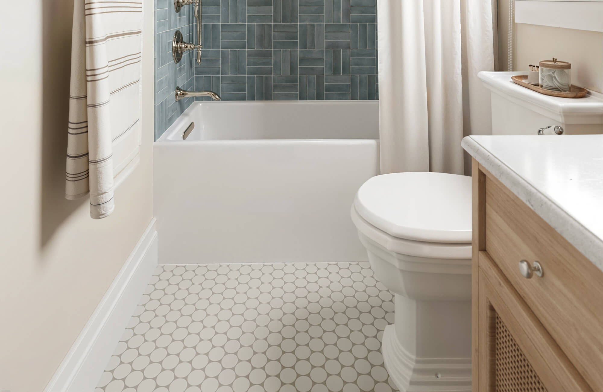 Bathroom featuring a blue tiled tub surround and light gray penny tile flooring beneath a white toilet and vanity.