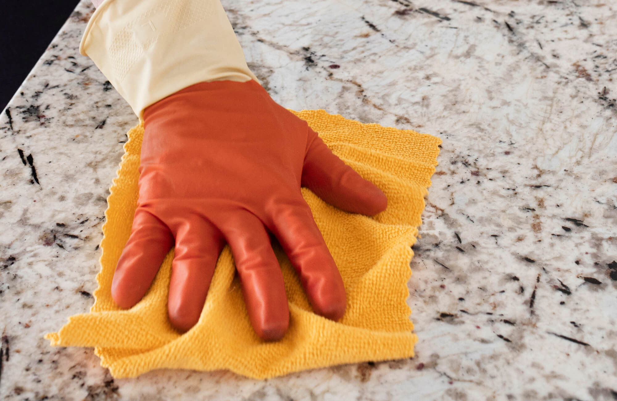 null Hand in a rubber glove, wiping a speckled marble table with a yellow cloth during cleaning.