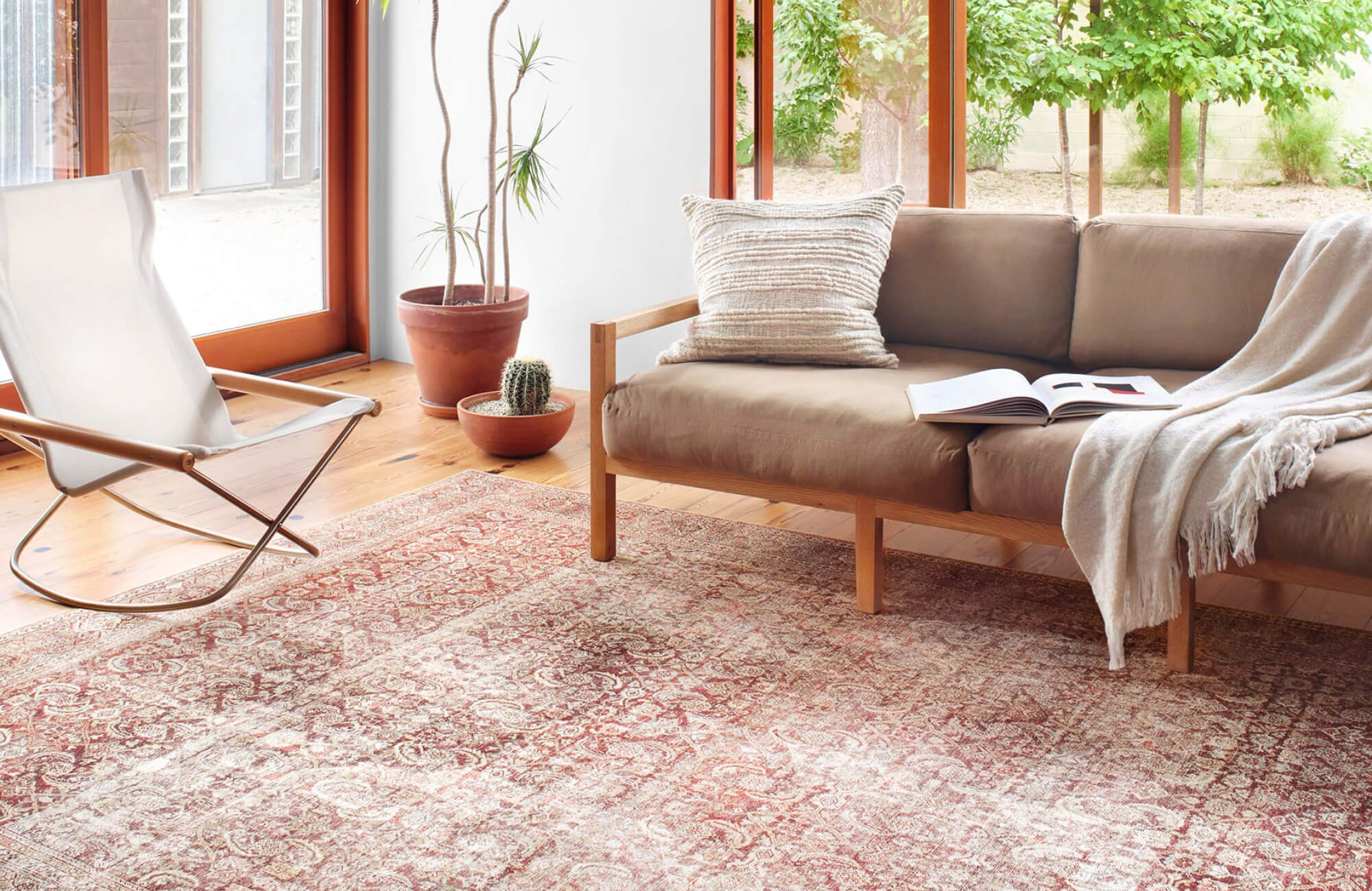 null Sunlit living space with red traditional Persian-style rug, intricate motifs adding warmth beneath mid-century sofa and natural wood tones.
