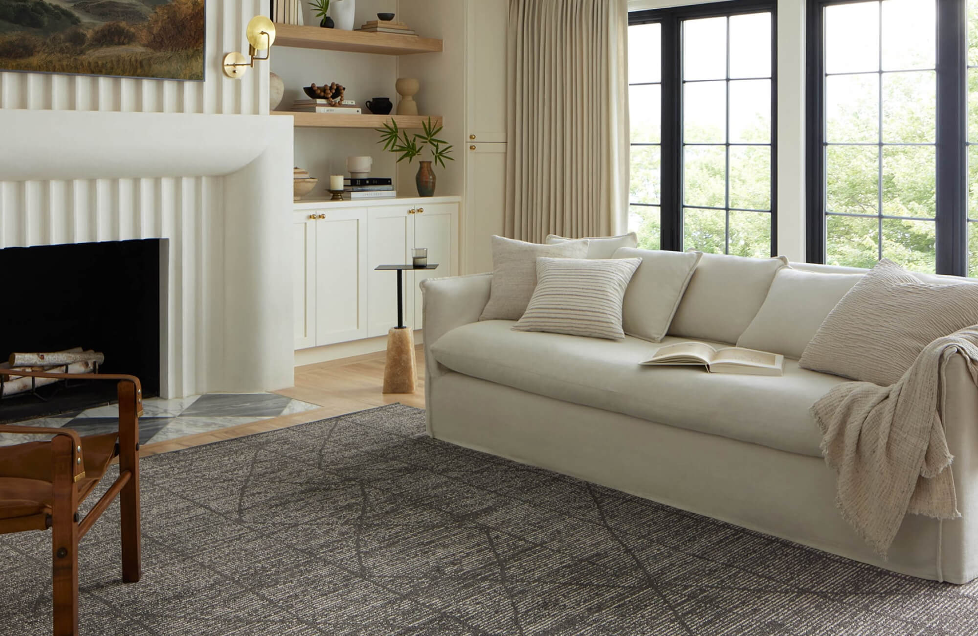 null Bright living room with charcoal geometric area rug, linear abstract pattern grounding a curved cream sofa and modern fireplace.