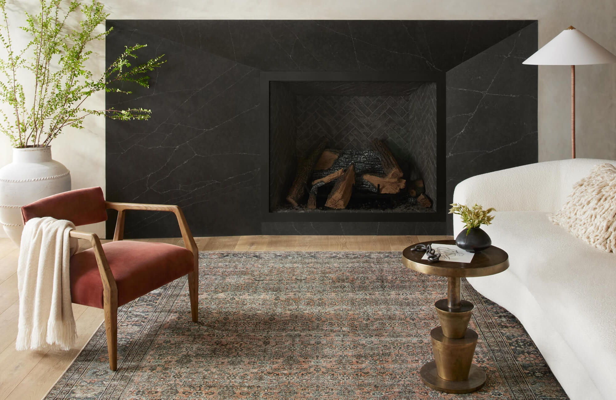 null Modern fireplace setting with faded traditional rug, muted red and blue motifs creating contrast against dark stone surround.