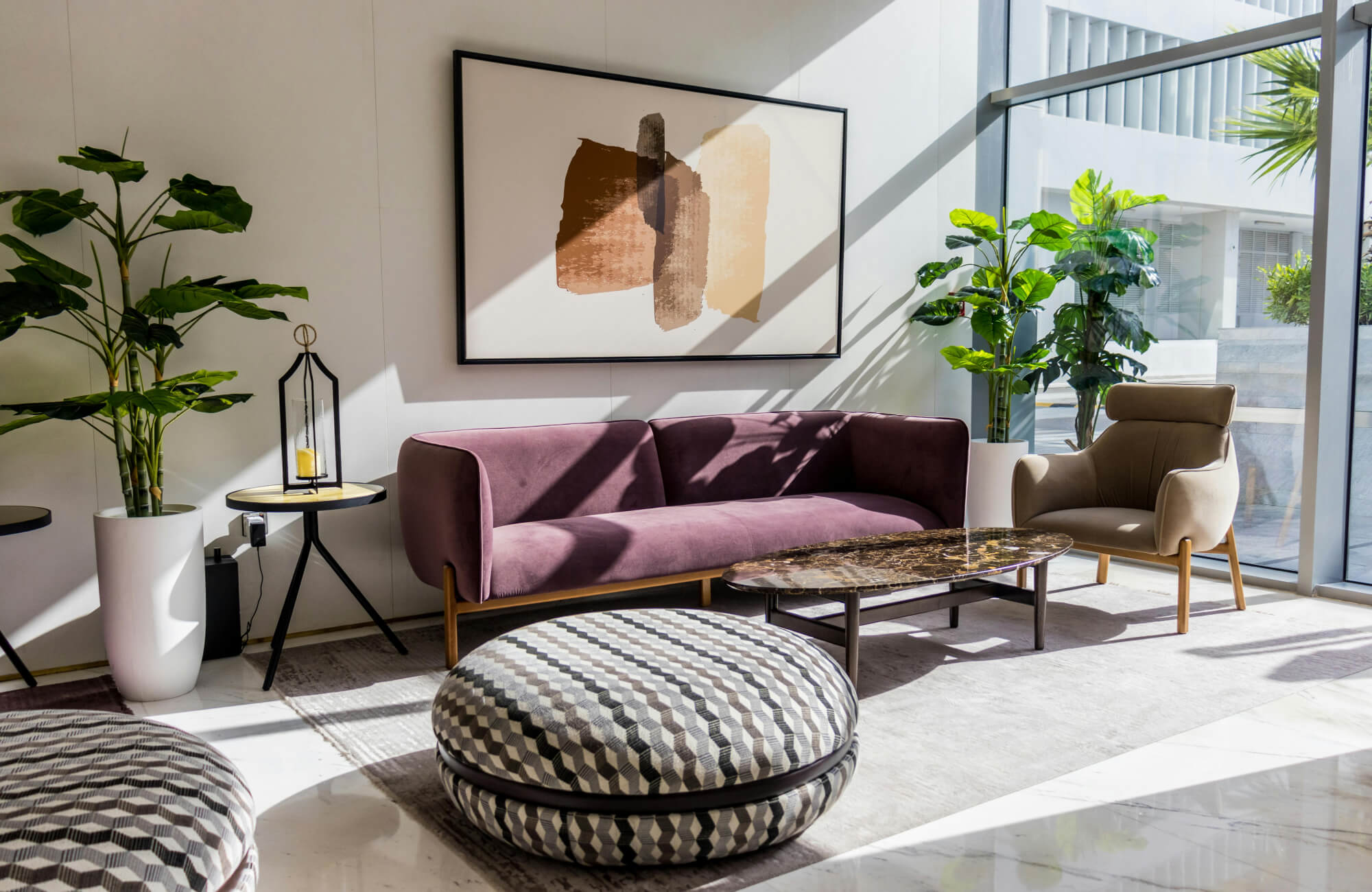 Oversized horizontal artwork above a sofa in a bright living room with large windows, creating visual continuity that makes the wall appear wider