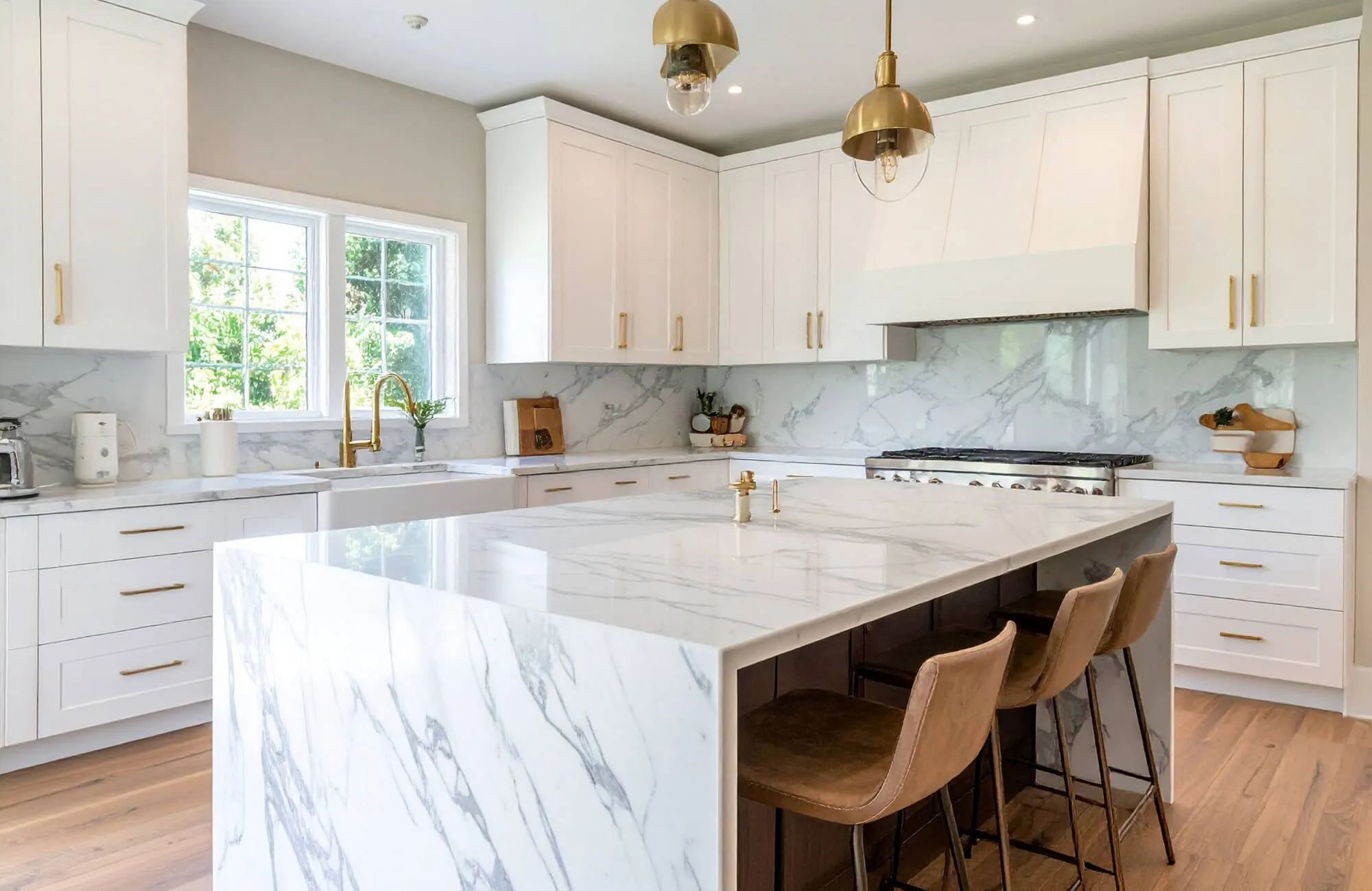 Bright kitchen with Calacatta marble waterfall island, white cabinetry, and warm brass pendants creating a refined, timeless look.