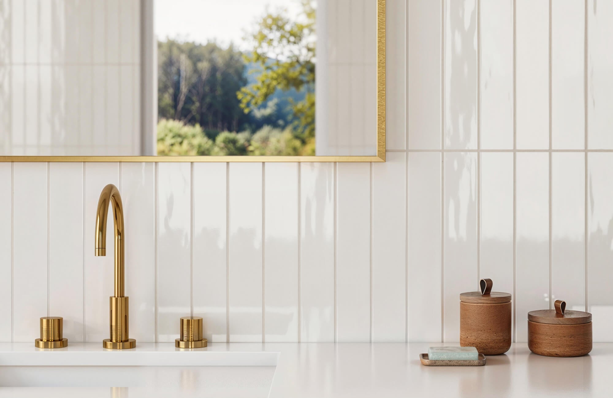 null Elegant bathroom featuring glossy white subway tiles, a modern brass faucet, and wooden canisters, all reflected in a gold-framed mirror with a scenic outdoor view.