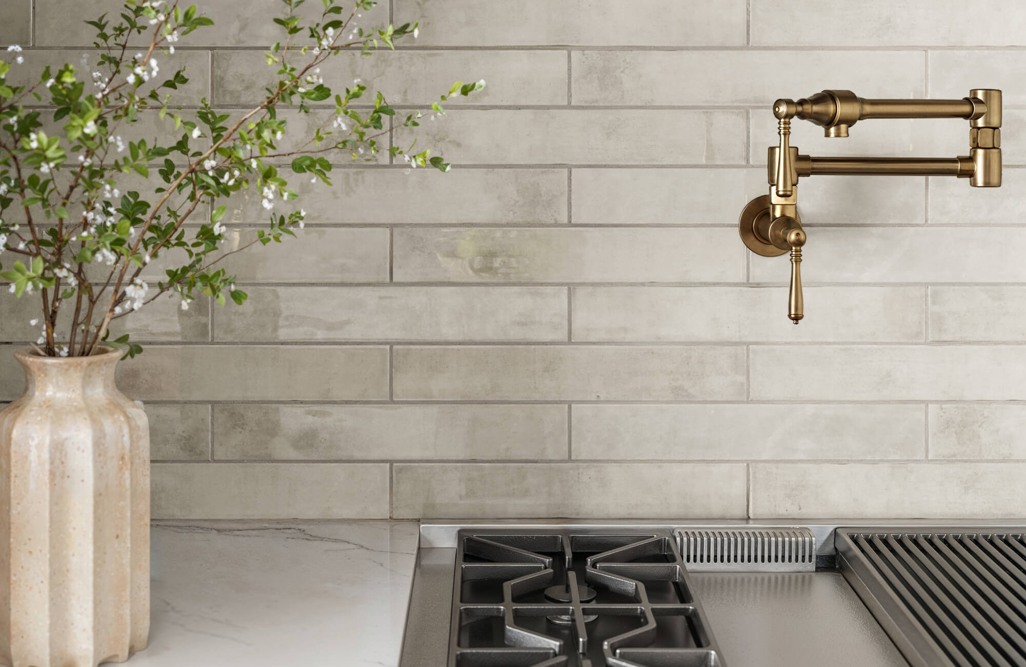 null Modern kitchen with light gray subway tiles, a brass pot filler faucet, and a ceramic vase holding a blooming branch, positioned next to a sleek gas stovetop.