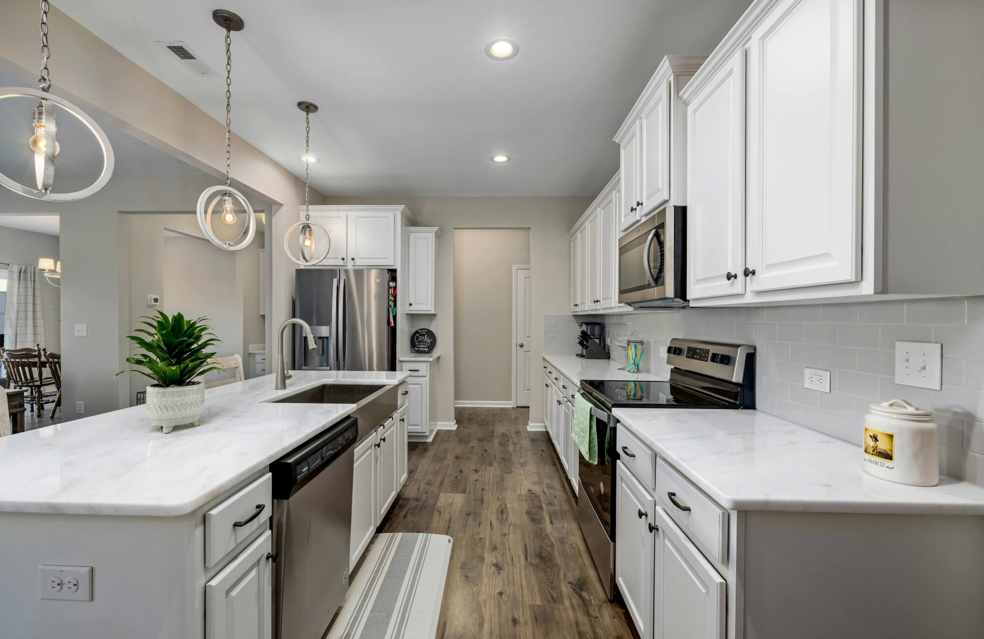 null Modern galley kitchen with ring pendant lights, wood flooring, and streamlined white cabinetry lining the walkway.