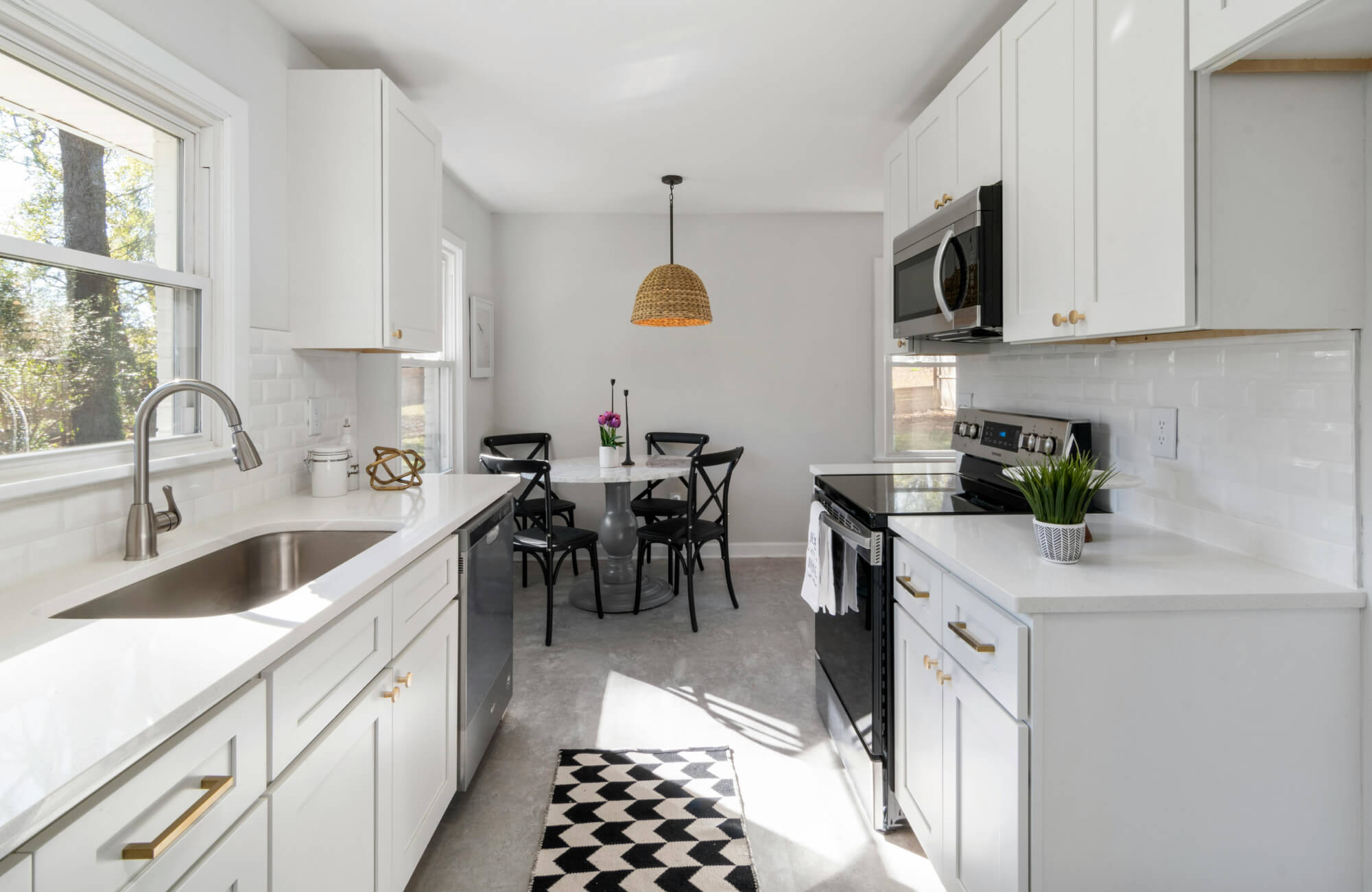 null Light-filled galley kitchen with a small dining nook, woven pendant light, and clean white cabinetry and counters.