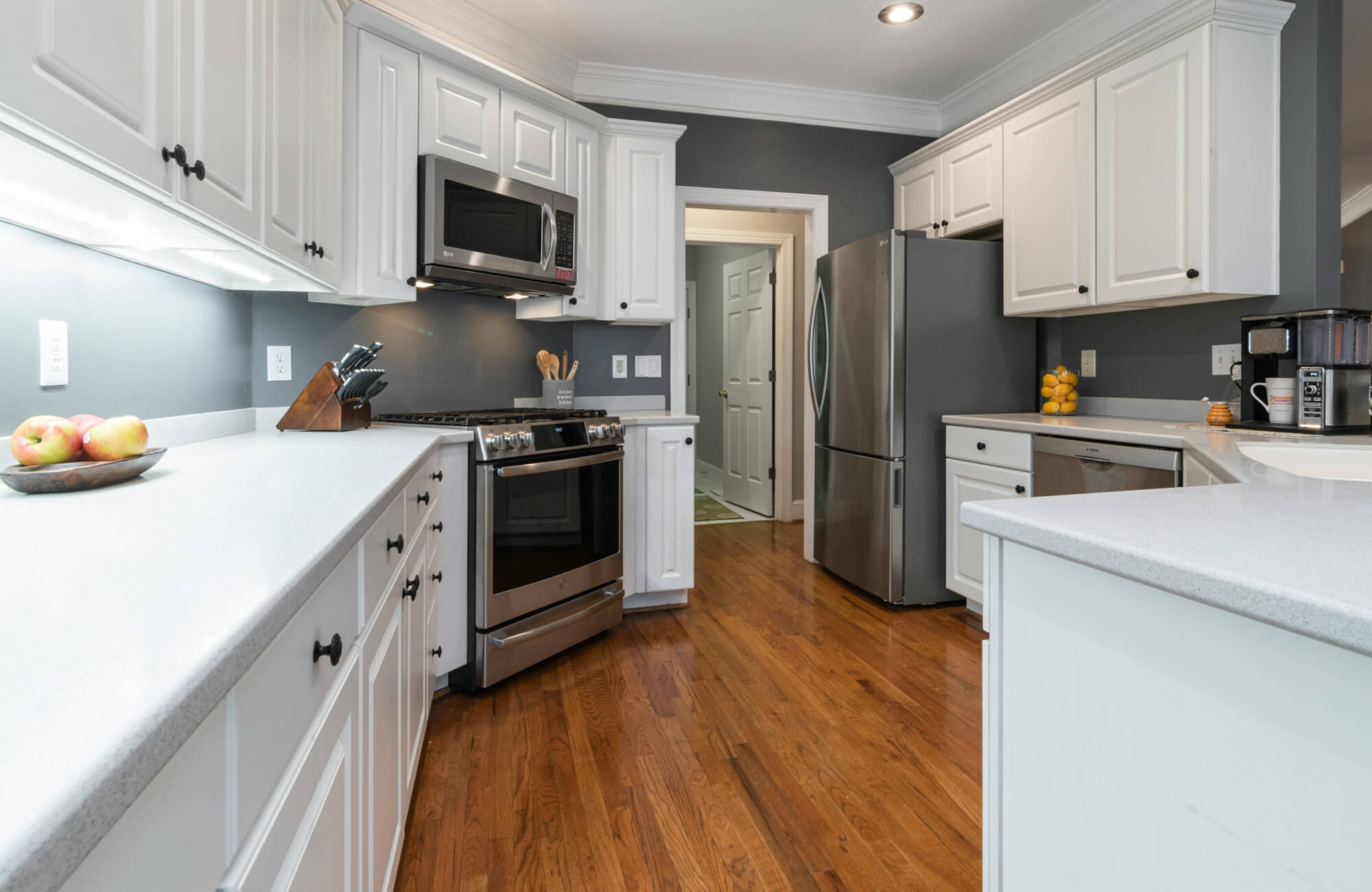 null Galley kitchen with white cabinets, wood floors, and soft under-cabinet lighting enhancing the narrow cooking space.