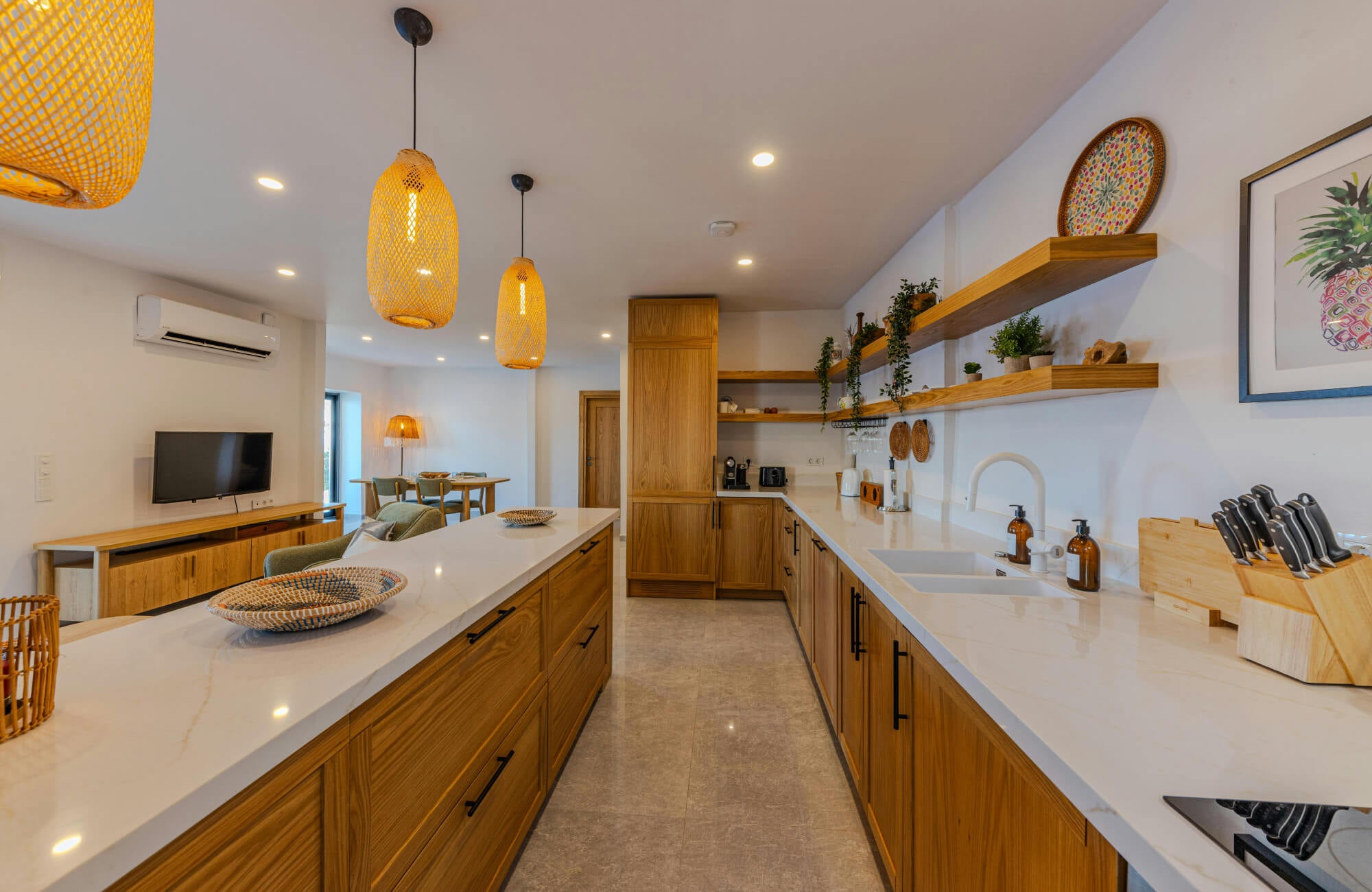null Warm galley kitchen with wood cabinets, large island seating, and woven pendant lighting brightening the long layout.